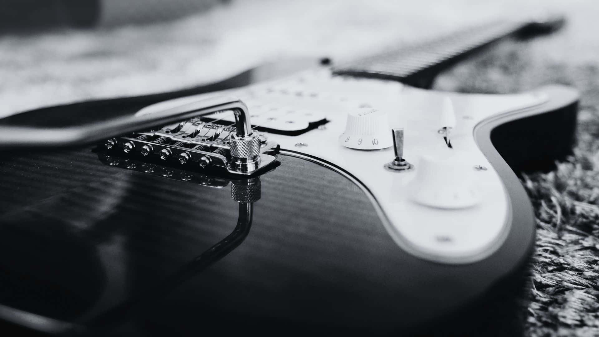 Black And White Guitar 桌布 壁紙 — 一張特寫黑白照片，拍攝一把時尚的電結他放在有紋理的地毯上，焦點銳利地落在其琴橋和旋鈕上。