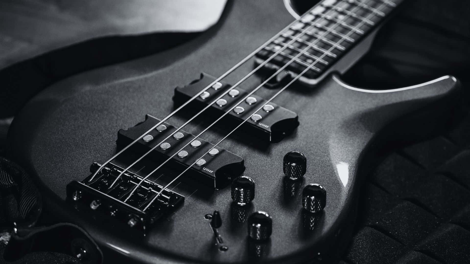 Black And White Guitar 桌布 壁紙 — 一張特寫黑白照片，拍攝一把時尚的低音結他放在有紋理的表面上，焦點銳利對準其弦線和旋鈕。
