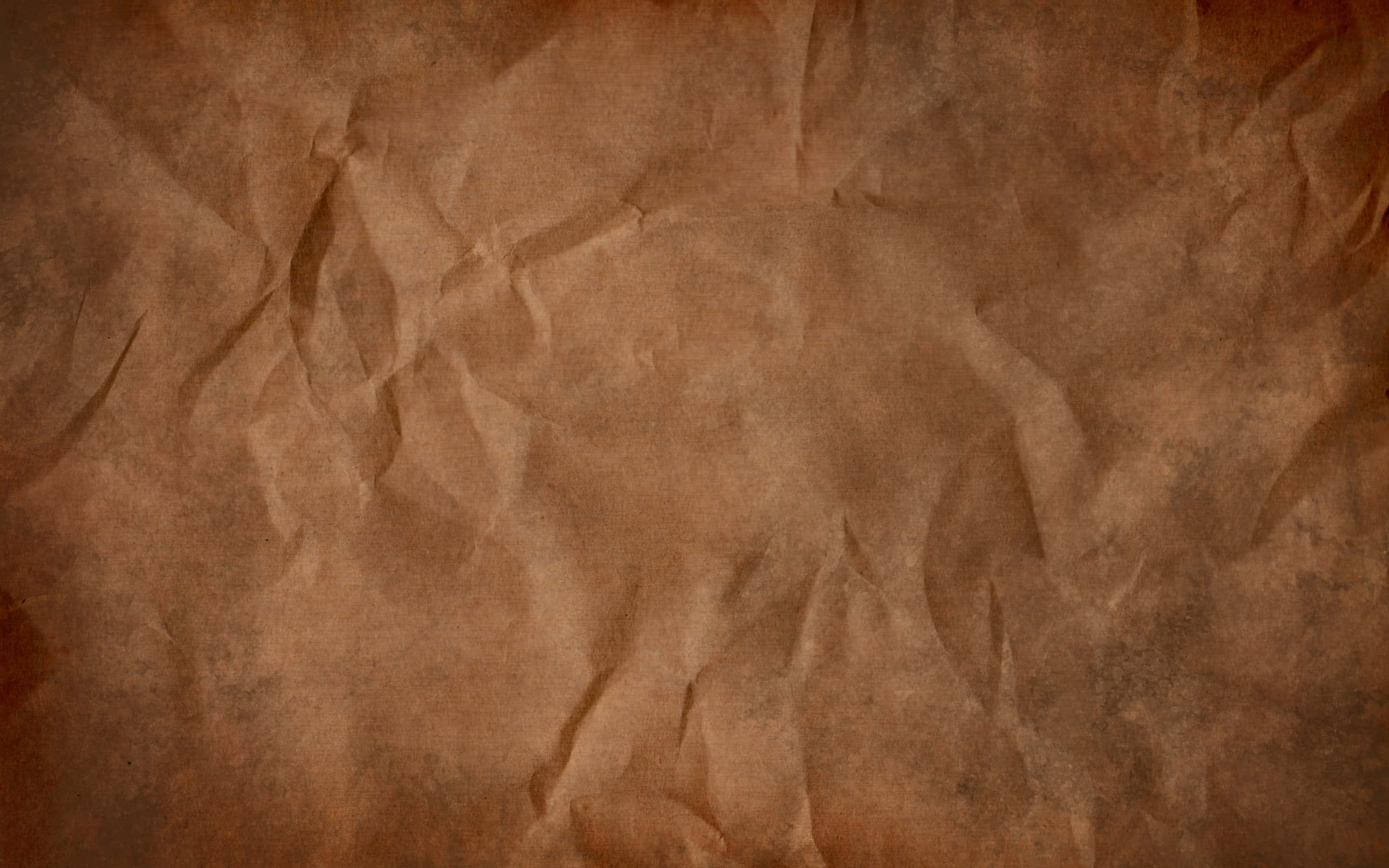 Brown Paper 桌布 壁紙 — 一張皺巴巴的棕色紙張特寫，帶有紋理摺痕和溫暖的大地色調。
