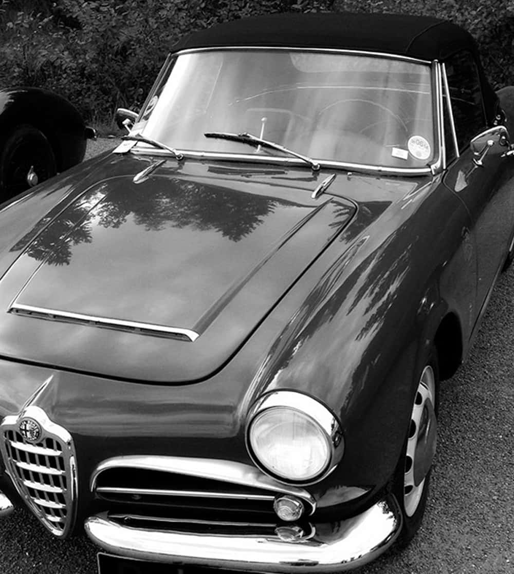 Car Hood 桌布 壁紙 — 一張經典黑白照片，一輛復古阿爾法羅密歐敞篷車停放在戶外，樹木倒映在其光亮的引擎蓋上。