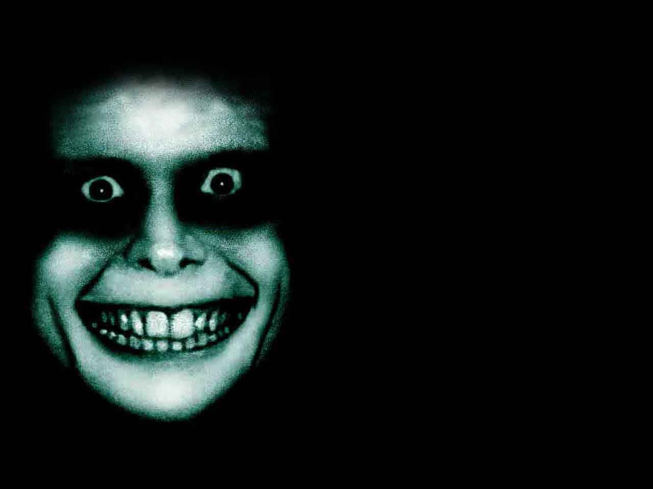 Freaky 桌布 壁紙 — 一張蒼白的鬼臉，睜大眼睛，露出牙齒的笑容，在陰森的綠色色調中從黑暗中浮現。
