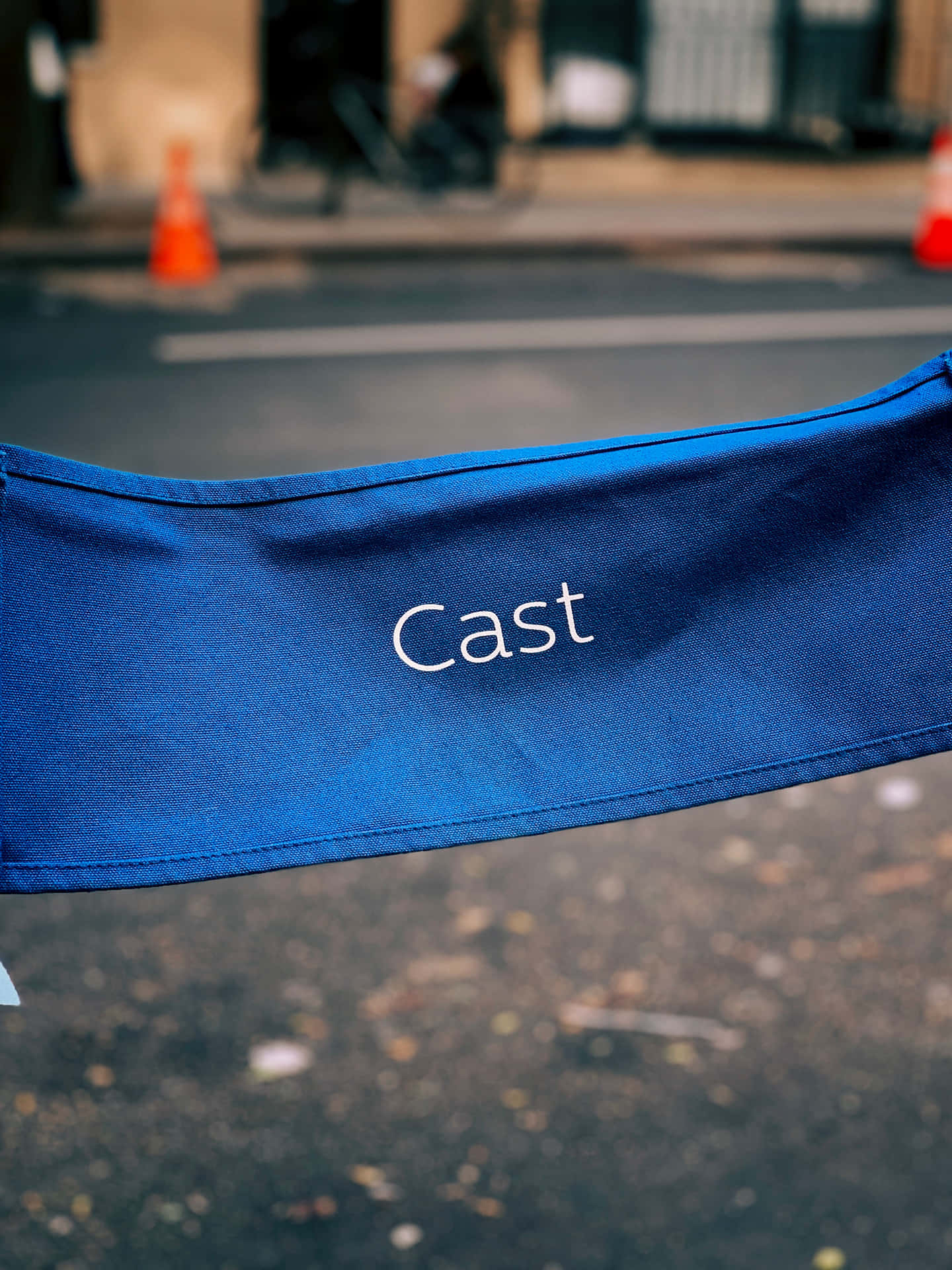 acting 桌布 壁紙 — 一張藍色導演椅的特寫，上面用白色繡有「Cast」字樣，背景是模糊的城市街道。