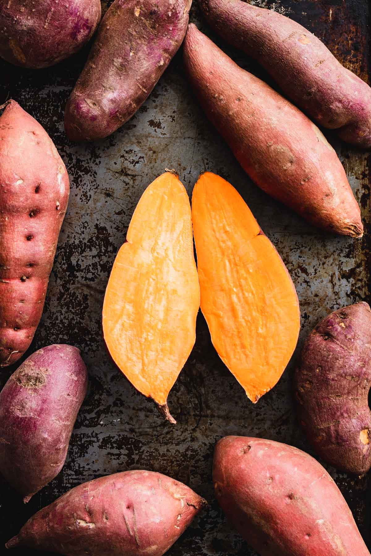 Potato 桌布 壁紙 — 一張質樸的俯拍照片，展示烤地瓜，帶有鮮豔的橙色果肉和紫色外皮，排列在一個風化的金屬托盤上。