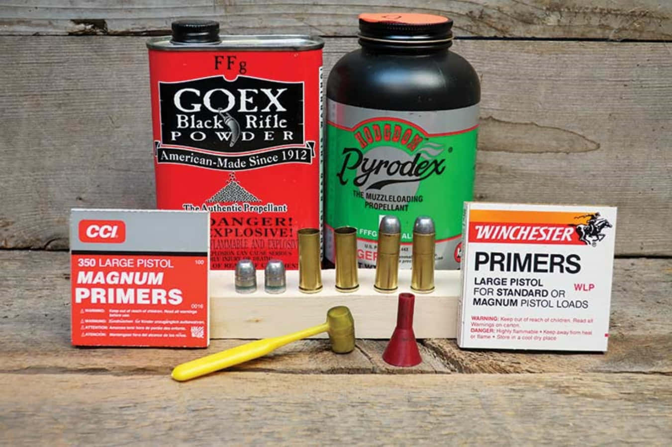 Black Powder 桌布 壁紙 — 一張質樸的木桌上展示著裝填用品，包括 Goex Black Powder Pyrodex 底火和黃銅彈殼，背景為風化的木材。