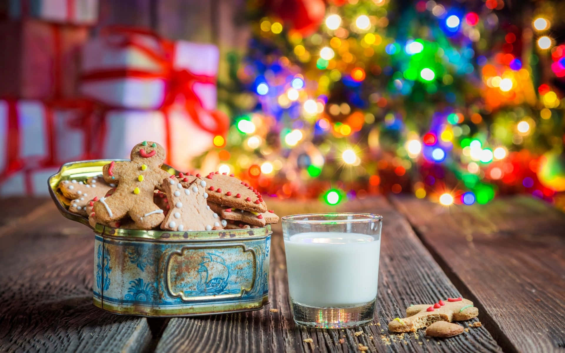 Winter Food 桌布 壁紙 — 一張質樸的木桌上放著一個復古罐子，裡面裝滿了薑餅曲奇，旁邊有一杯牛奶，背景是模糊的聖誕樹，掛滿了彩色燈飾。