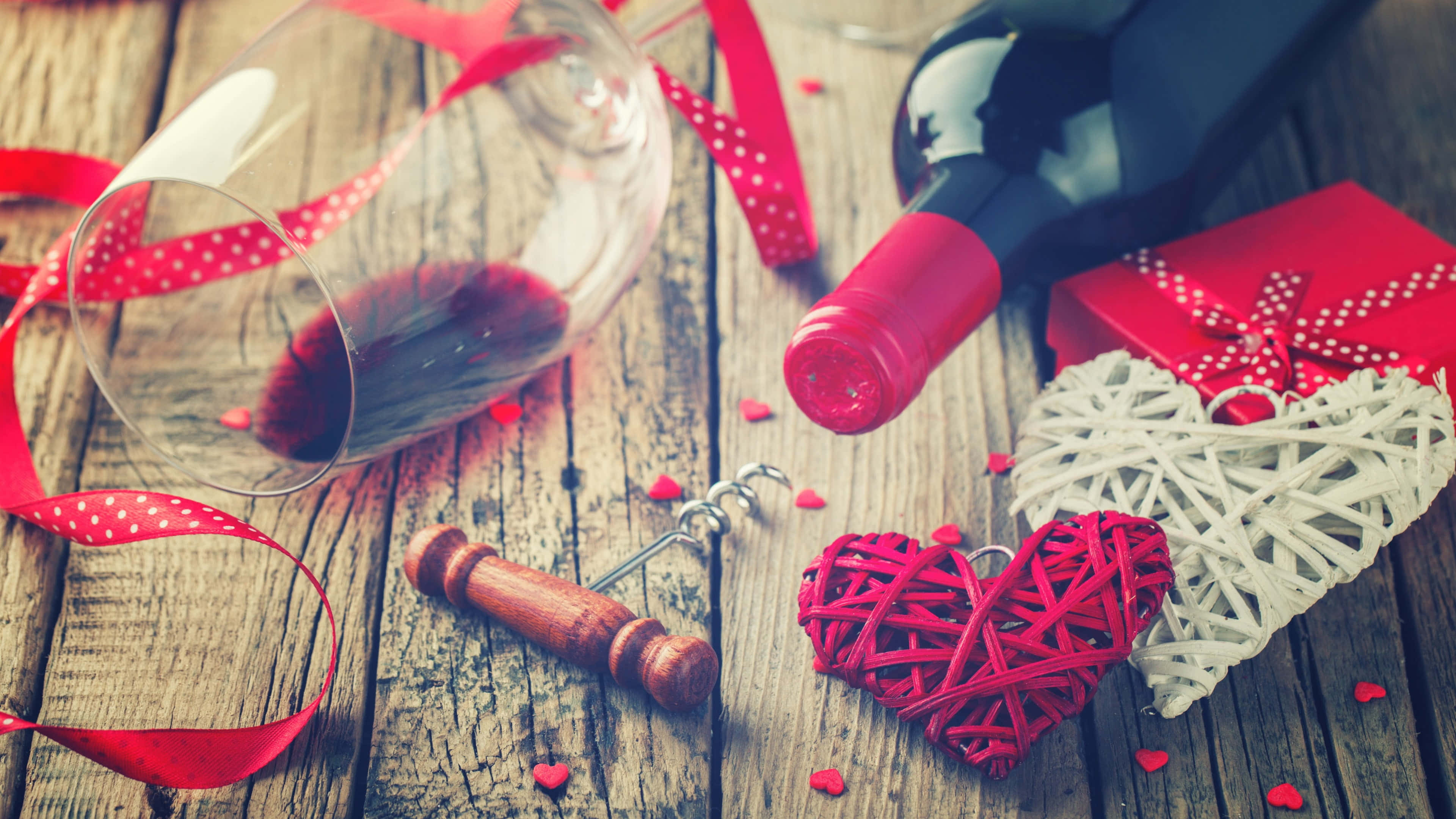 4K Love 桌布 壁紙 — 一張質樸的木桌上放著一個酒瓶、玻璃杯、開瓶器，以及用紅絲帶裝飾的編織心形和散落的紙心。