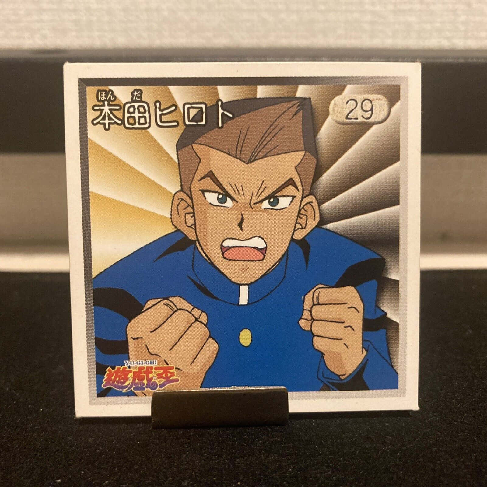 Tristan Taylor 桌布 壁紙 — 一張遊戲王集換式卡牌的特寫，卡上有一位身穿藍色制服、握緊拳頭、神情堅定的動漫角色。