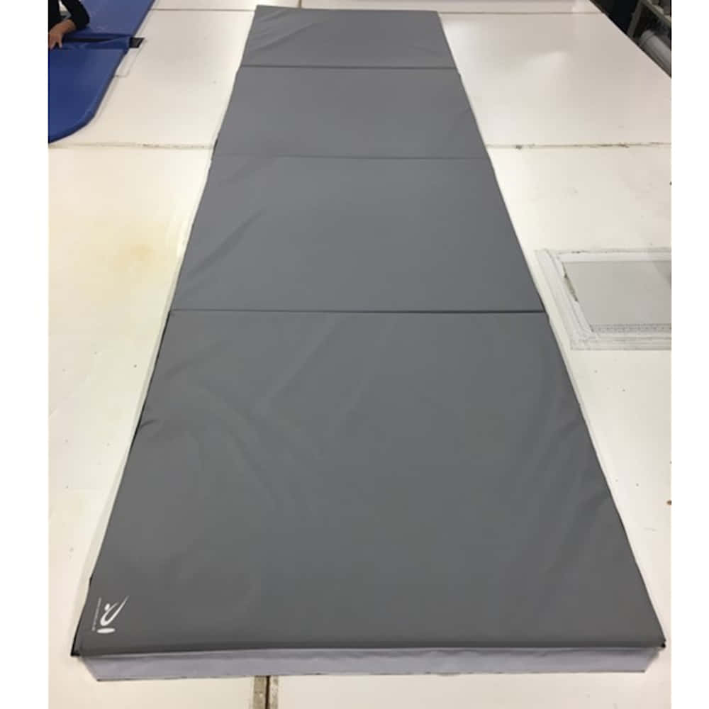 Gymnastics Mat 桌布 壁紙 — 一張長灰色體操墊鋪在健身房的白色瓷磚地板上，附近隱約可見一個人。