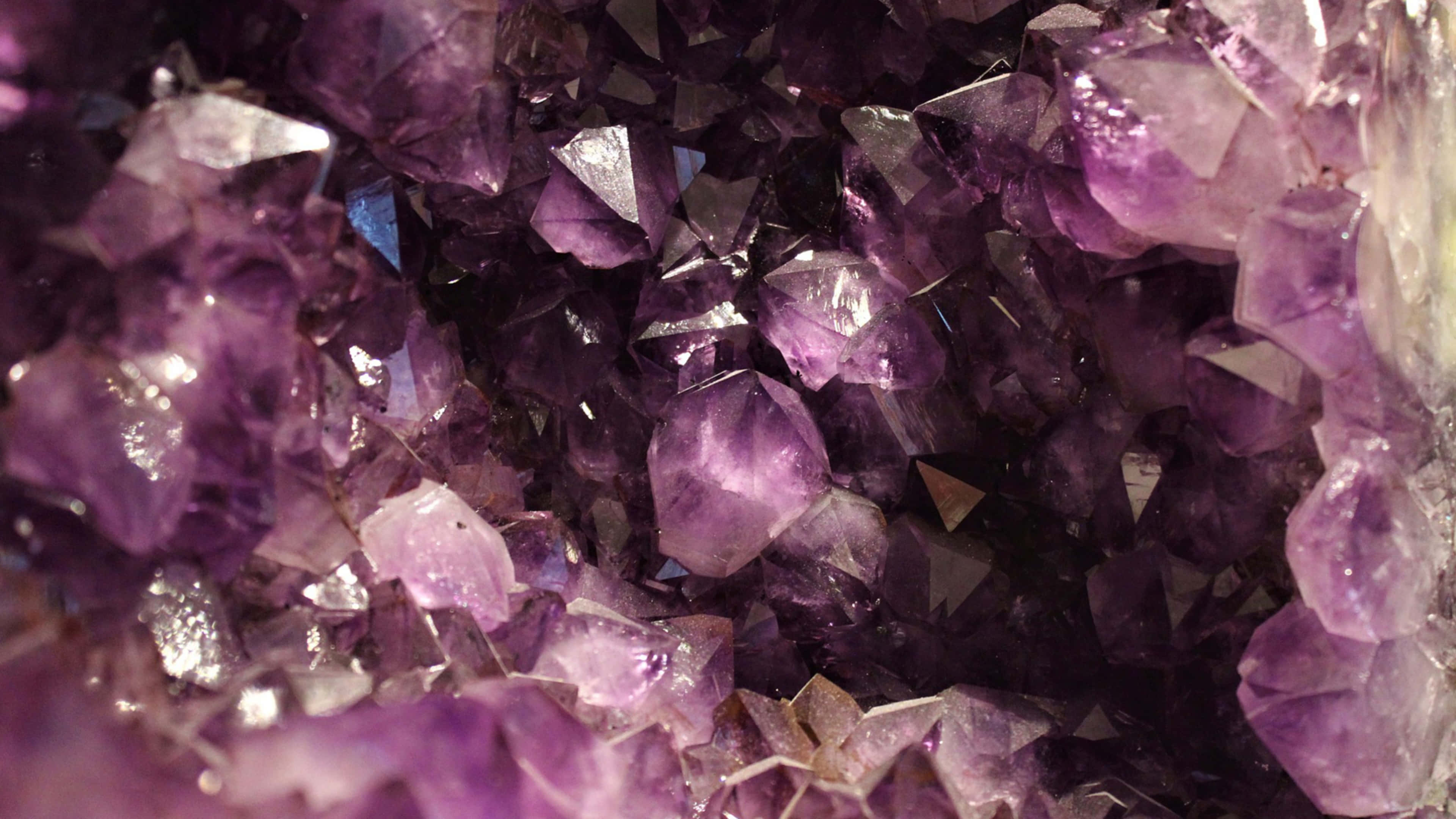 Amethyst 桌布 壁紙 — 一張閃爍紫色紫水晶晶體的近距離照片，形成密集、閃閃發光的簇狀，具有銳利的刻面和深紫羅蘭色調。