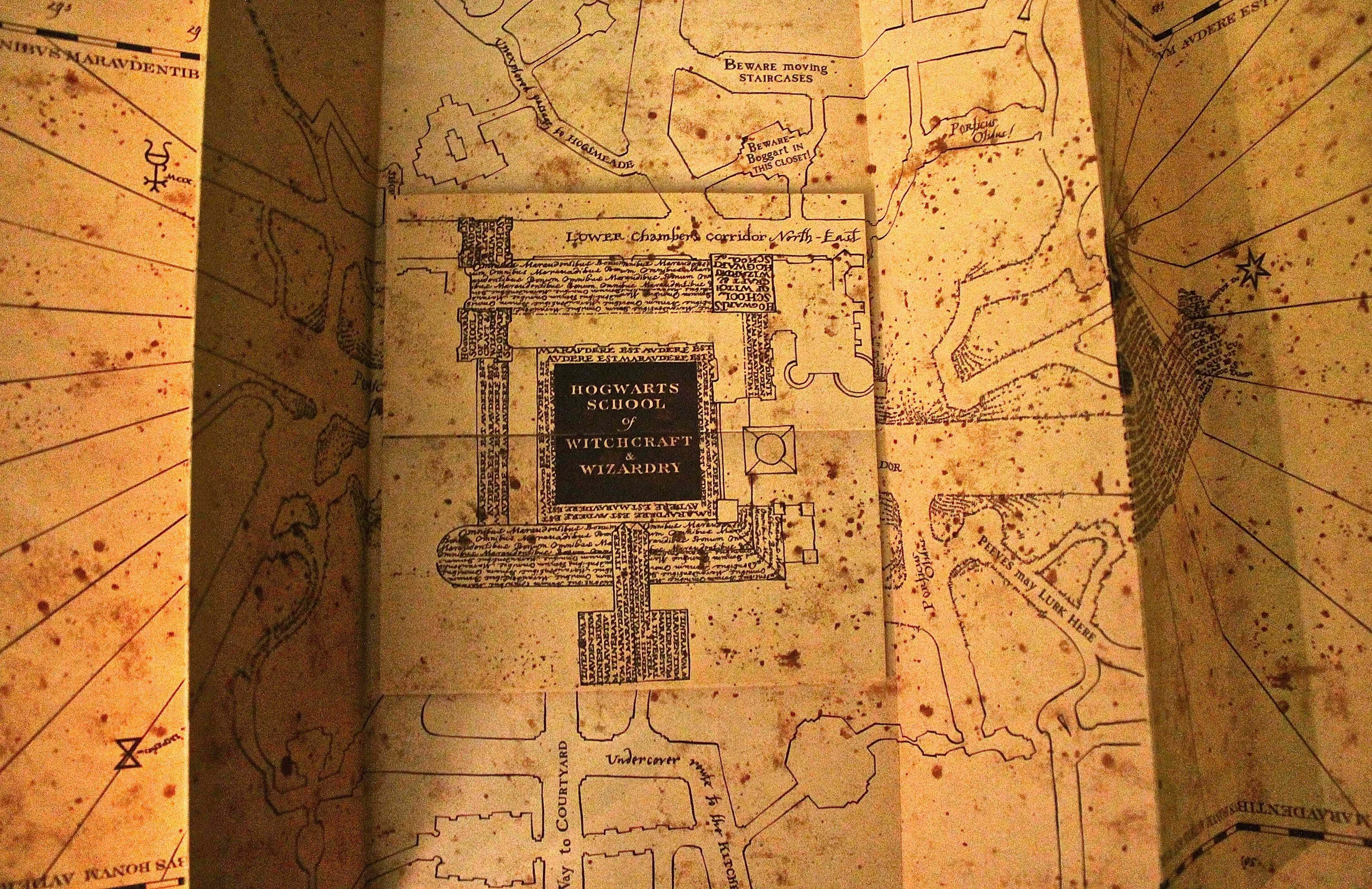 The Marauder's Map 桌布 壁紙 — 一張陳舊、有污漬的霍格華茲地圖在溫暖燈光下展開，顯露出詳細的走廊和手寫警告。