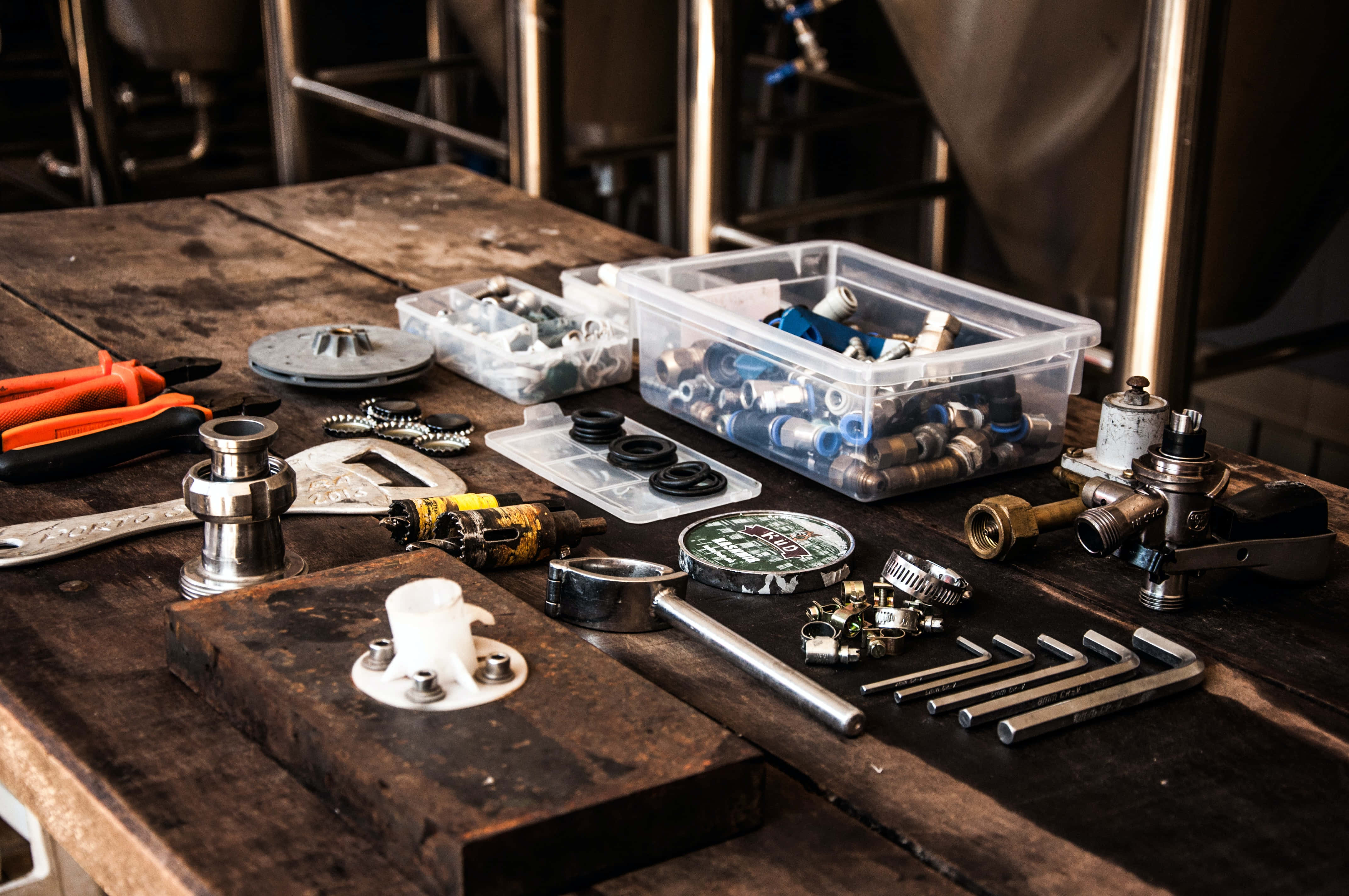 Plumbing 桌布 壁紙 — 一張雜亂的木製工作枱上，在溫暖的方向性燈光下，擺放著一系列機械工具和零件。