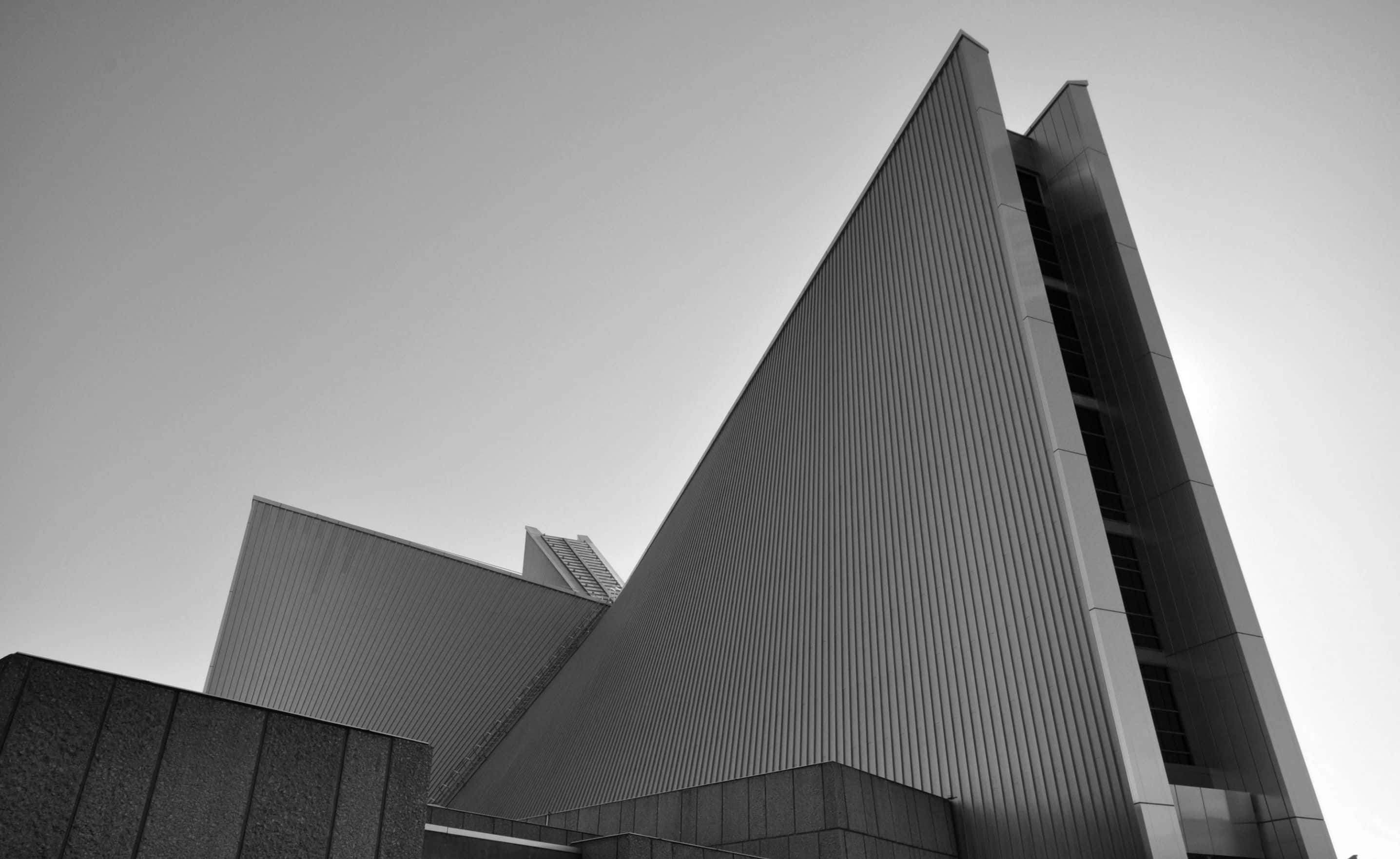Black And White Architecture 桌布 壁紙 — 一張鮮明的黑白低角度照片，呈現棱角分明的現代主義建築刺穿蒼白的天空。
