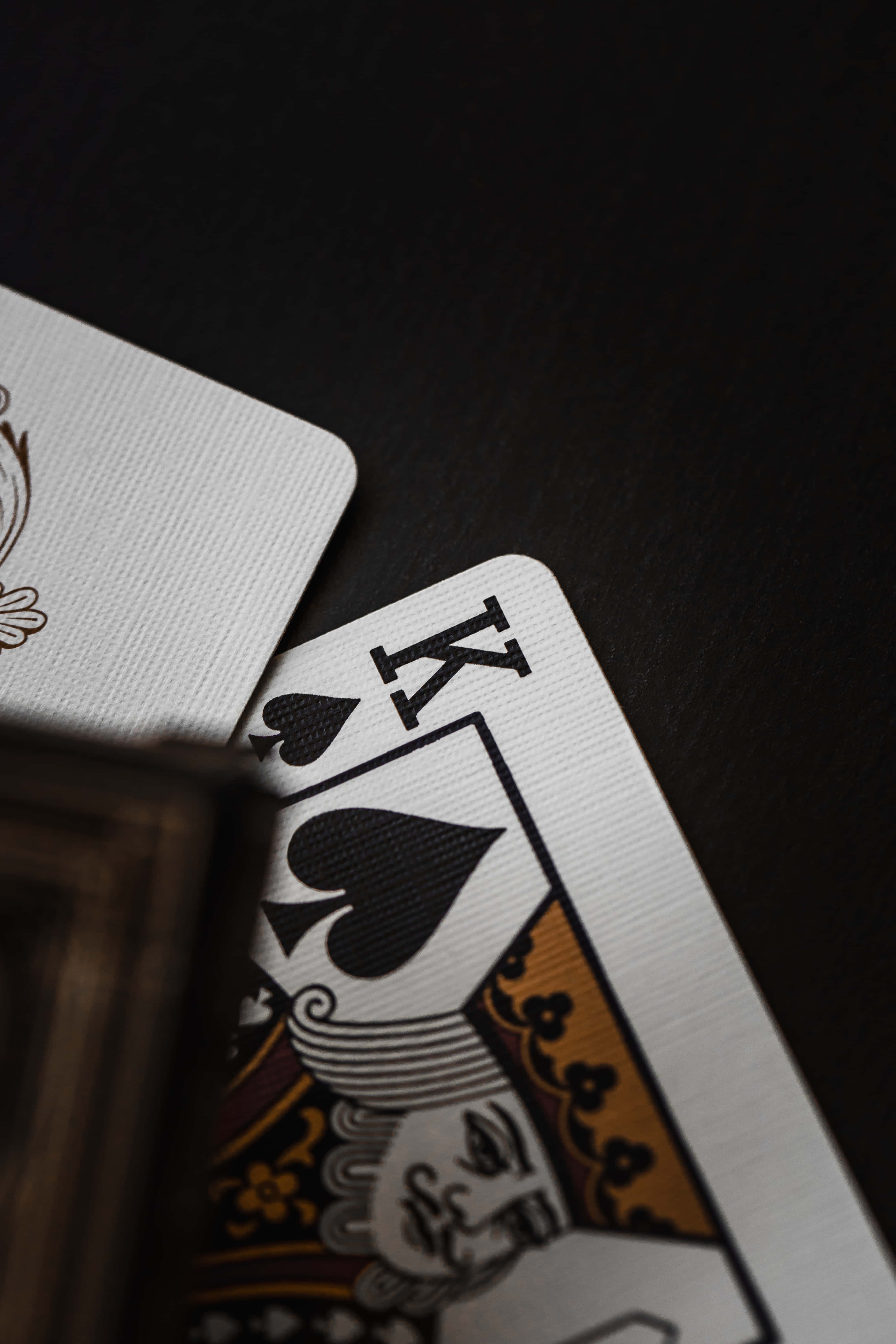 Playing Cards 桌布 壁紙 — 一張黑桃K啤牌局部重疊在另一張牌上，置於深色紋理表面的特寫。