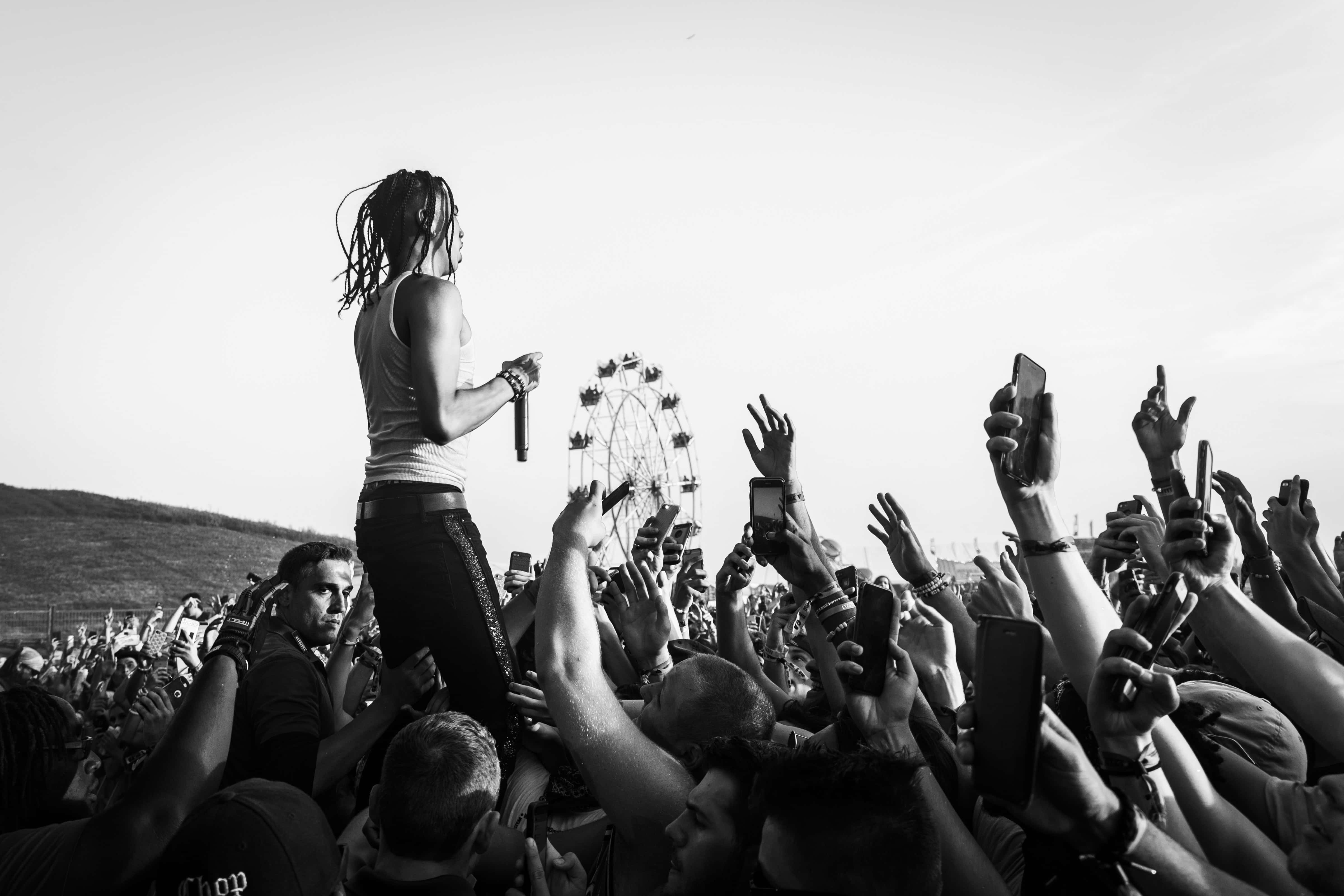 music festival 桌布 壁紙 — 一張黑白照片，一名梳著辮子頭的表演者在戶外音樂節的人群上方對著麥克風唱歌，背景有摩天輪。