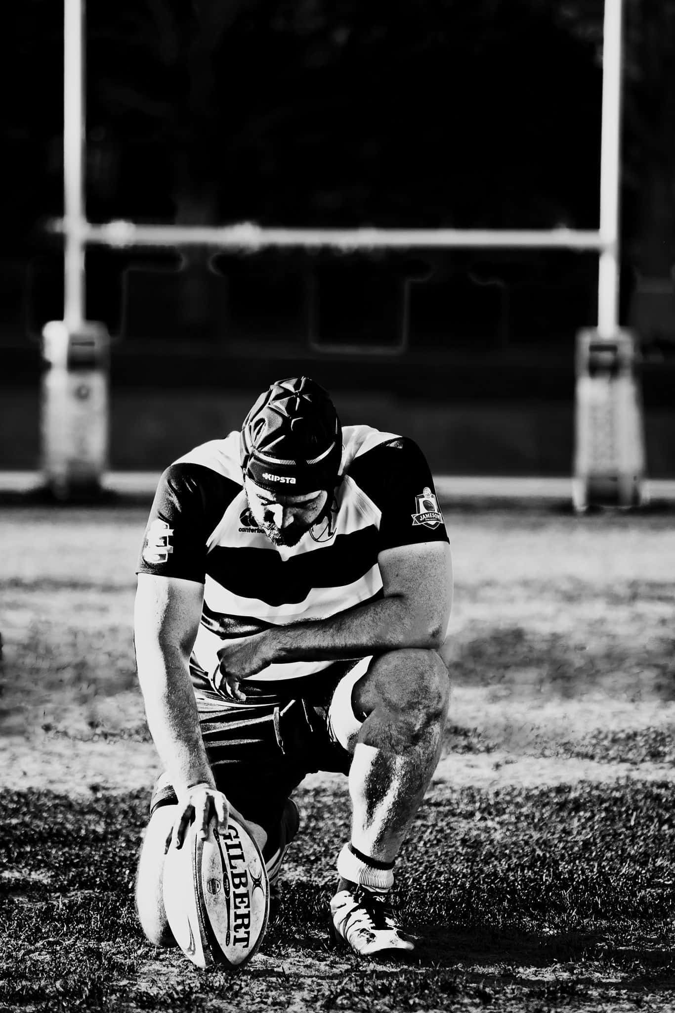 Scotland Rugby 桌布 壁紙 — 一張黑白照片，一名欖球運動員跪在草地上，低頭抱球，顯得筋疲力盡。
