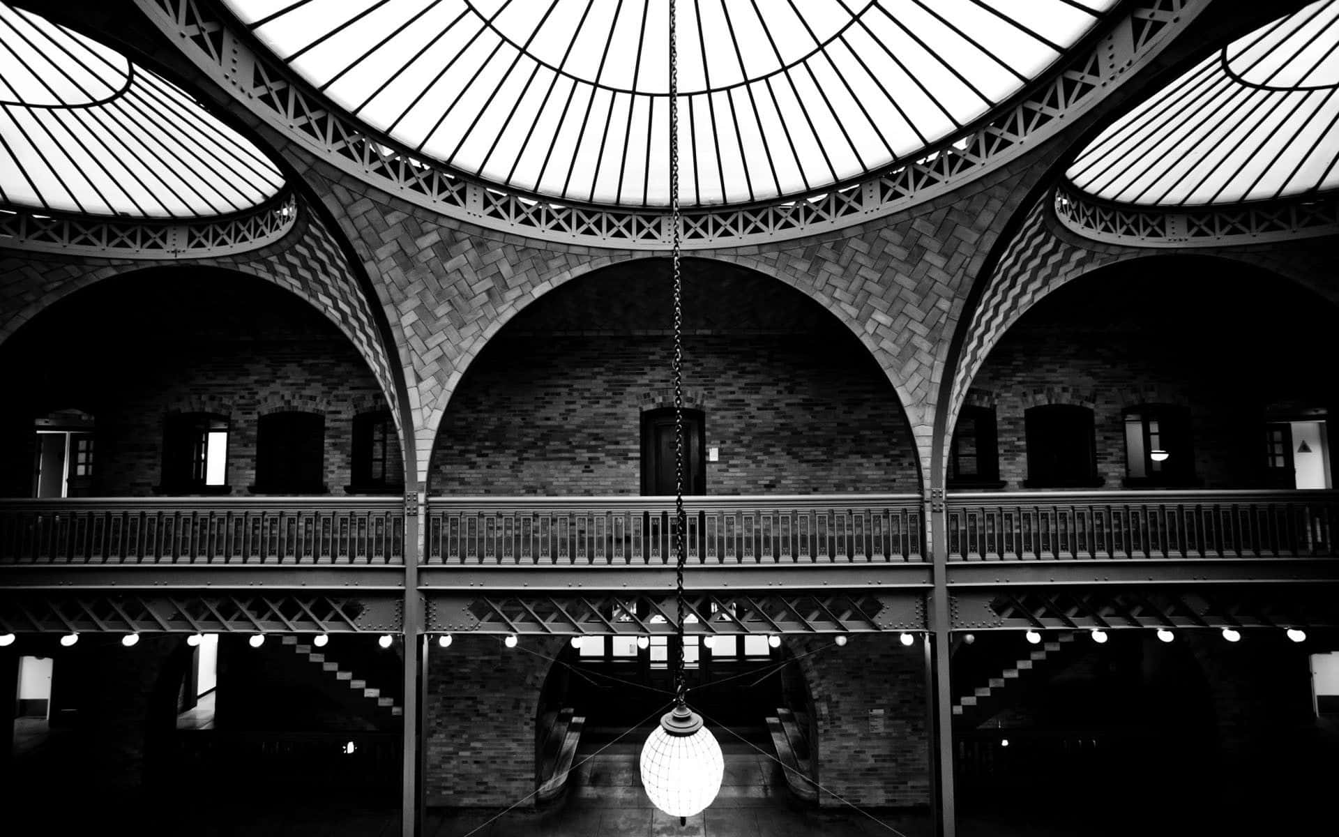 Black And White Architecture 桌布 壁紙 — 一張黑白照片，展示了一個宏偉的拱形磚砌中庭，帶有玻璃穹頂天花板和一個懸掛的球形燈具。