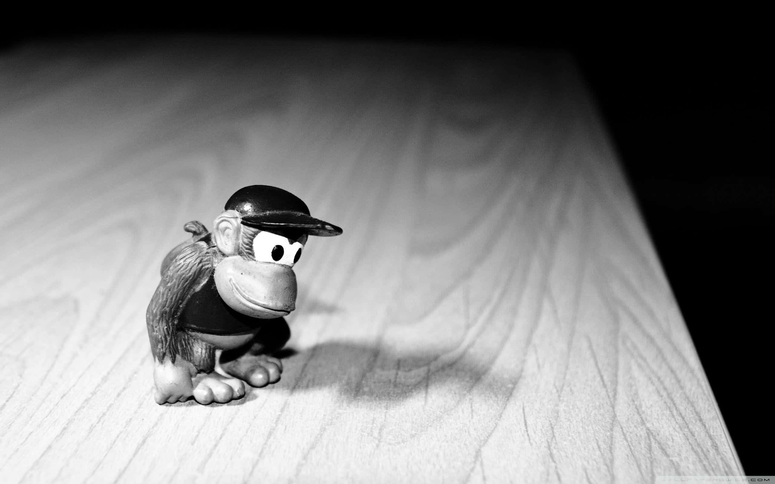 Diddy Kong 桌布 壁紙 — 一張黑白照片，拍攝了一隻戴著帽子的小猴子雕像，放在木質表面上，光線效果強烈。