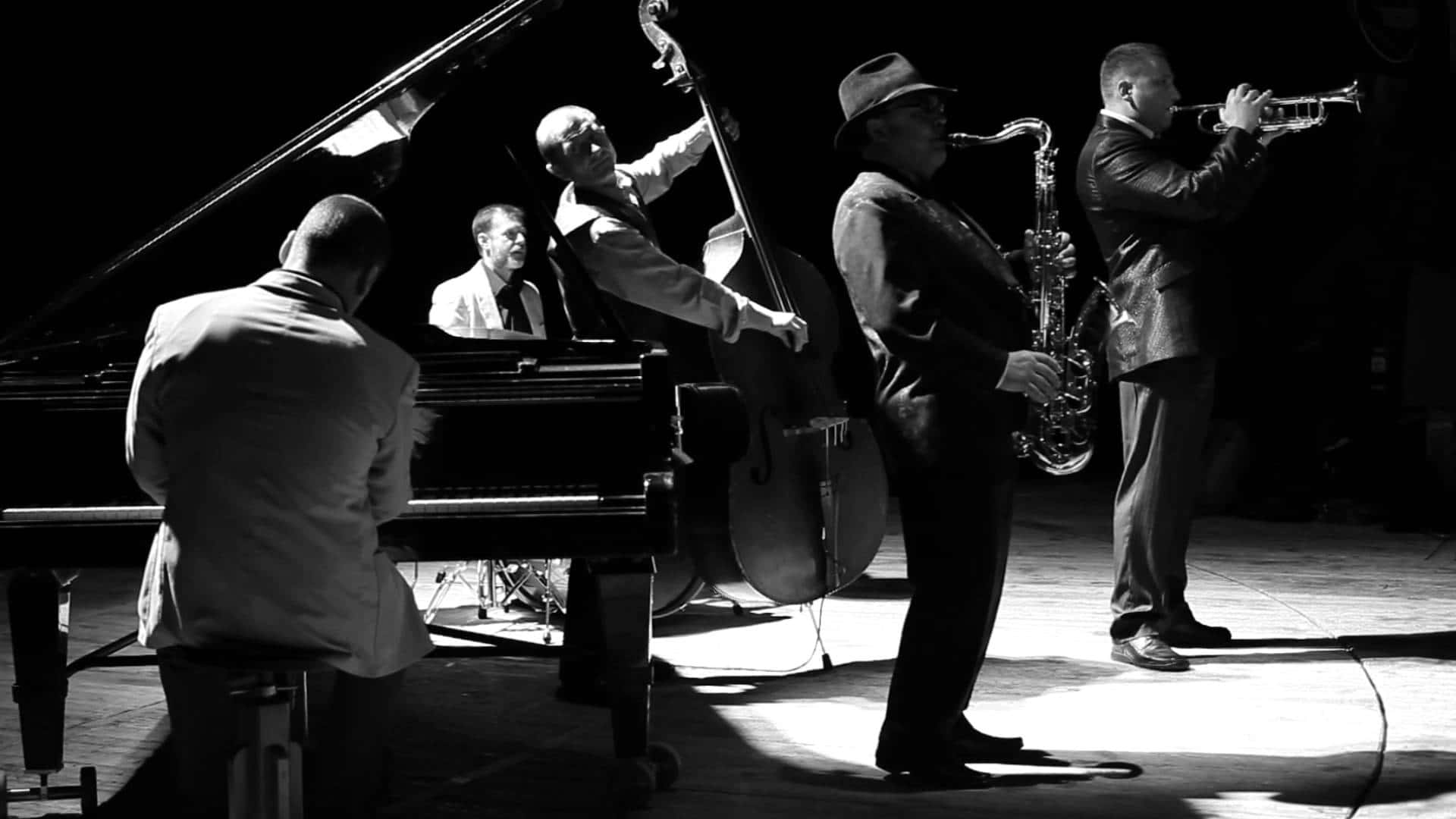Jazz 桌布 壁紙 — 一張黑白照片，爵士樂隊在舞台上表演，帶有戲劇性的聚光燈效果。