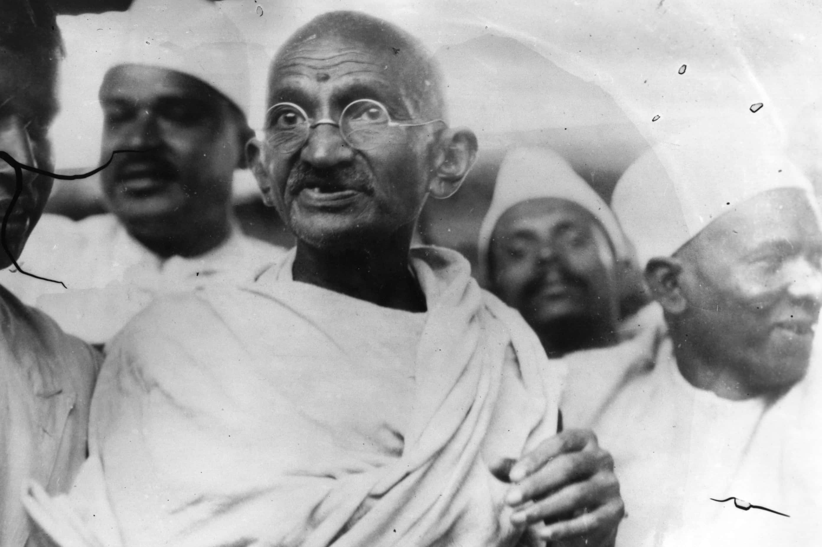 Mahatma Gandhi 桌布 壁紙 — 一張黑白照片，顯示聖雄甘地戴著圓形眼鏡和穿著腰布，被戴著頭巾的男人包圍。