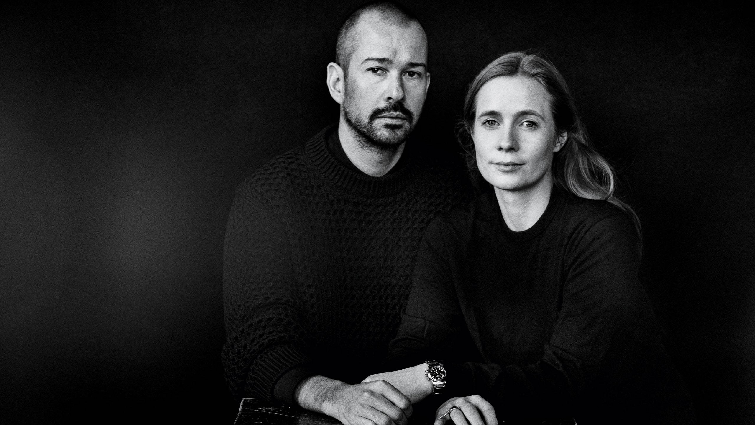 Jil Sander Luke & Lucie Meier 壁紙 — 一張黑白肖像，一男一女緊靠著坐在深色背景前，表情嚴肅。