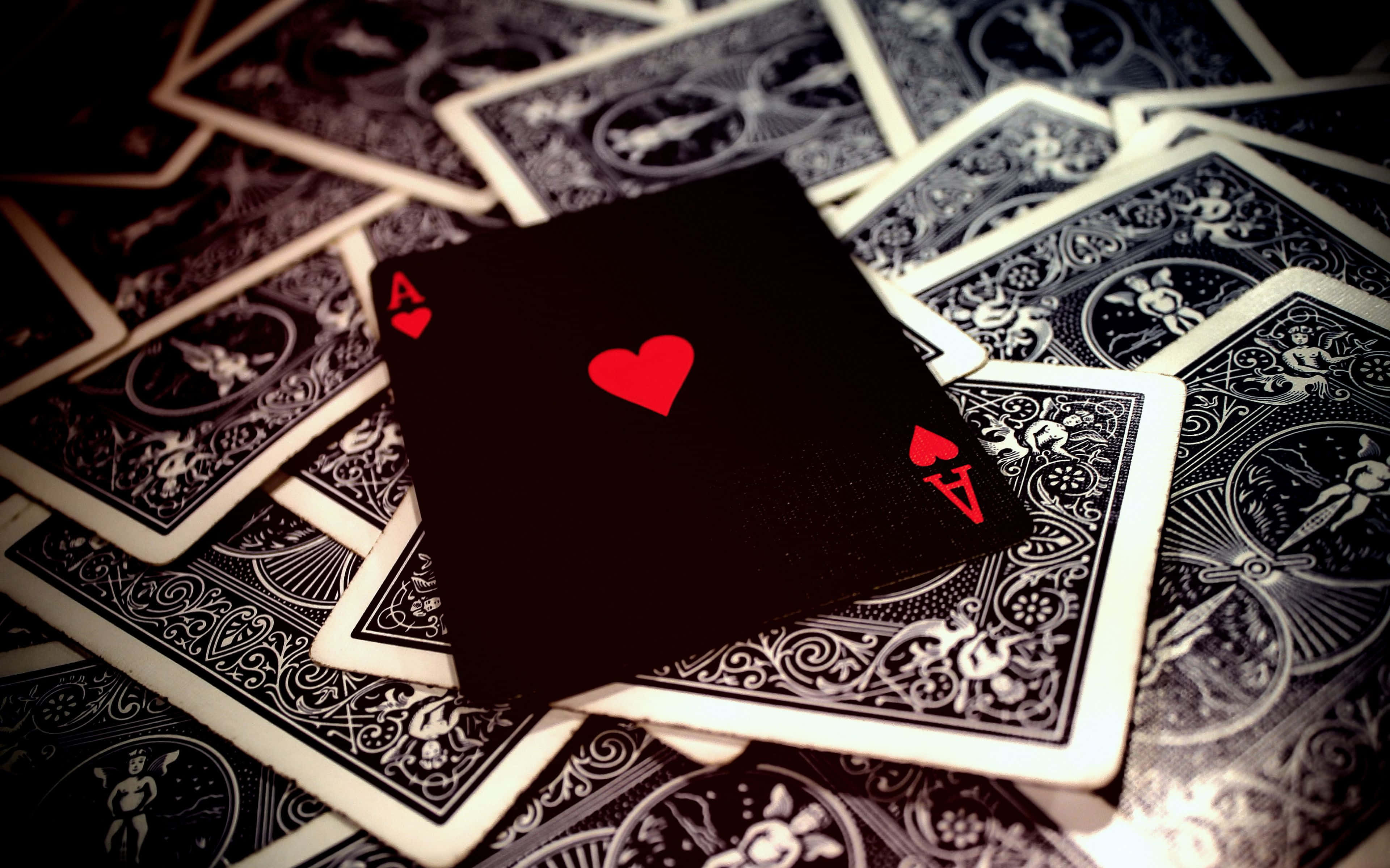 Card Games 桌布 壁紙 — 一張黑色紅心Ace牌放在一堆散落、帶有複雜白色圖案的精美撲克牌之上。