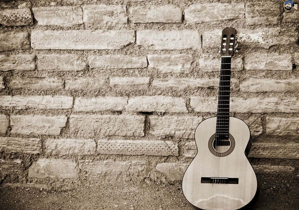 Musical 桌布 壁紙 — 一把古典結他靠喺一幅風化嘅石牆上，呈現懷舊嘅啡色調構圖。