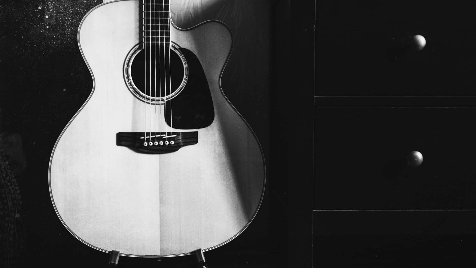 Black And White Guitar 桌布 壁紙 — 一把單色原聲結他靠在一個帶有圓形把手嘅深色抽屜櫃上，身處簡約工作室環境。