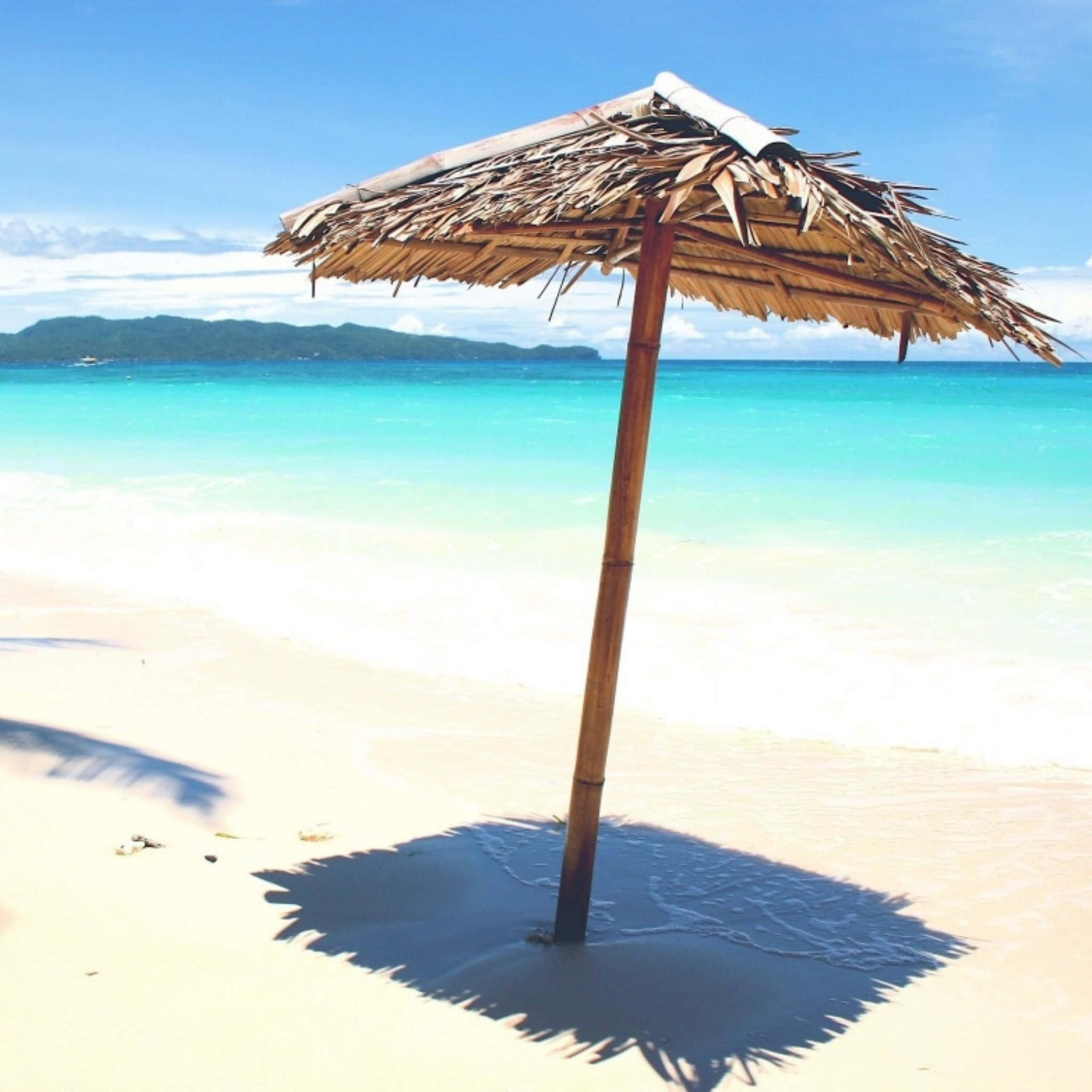 Beach Umbrella 桌布 壁紙 — 一把孤獨的茅草沙灘傘在白色沙灘上投下陰影，碧綠色的海浪在清澈的藍天下拍打著海岸。