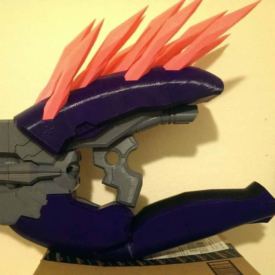 Halo Needler 桌布 壁紙 — 一把定製的3D打印科幻武器，帶有紫色握把和珊瑚紅色尖刺，放在一個紙板箱上，背景是米色牆壁。
