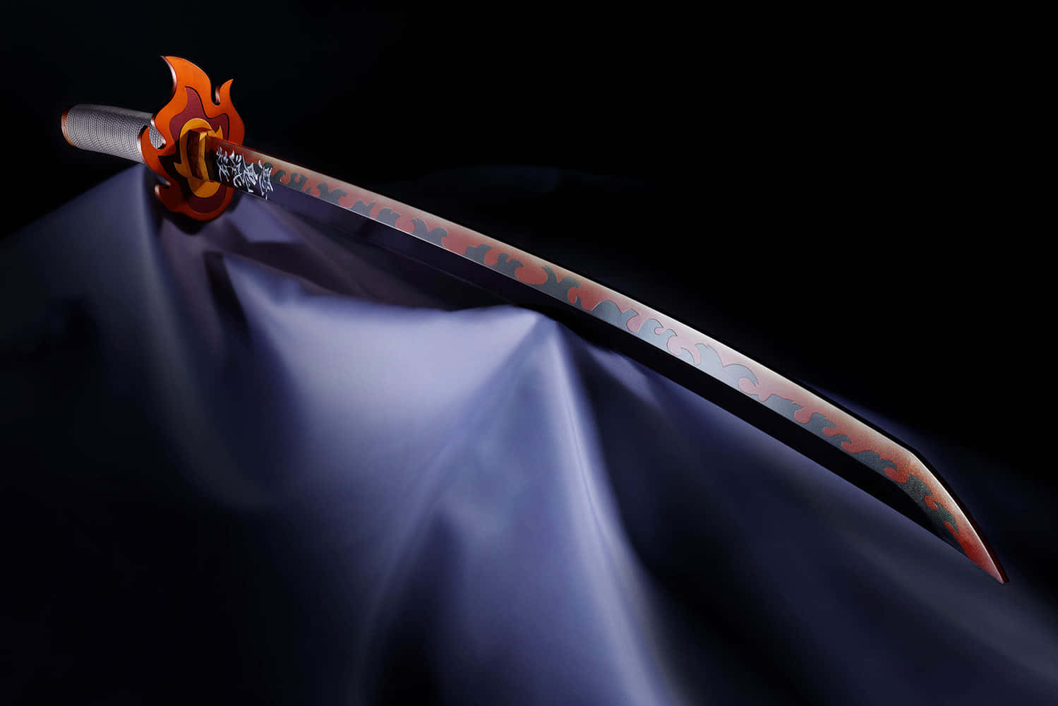 Rengoku Sword 桌布 壁紙 — 一把帶有火焰圖案的熾熱橙色劍柄劍斜放在黑色背景前的靛藍色布料上。