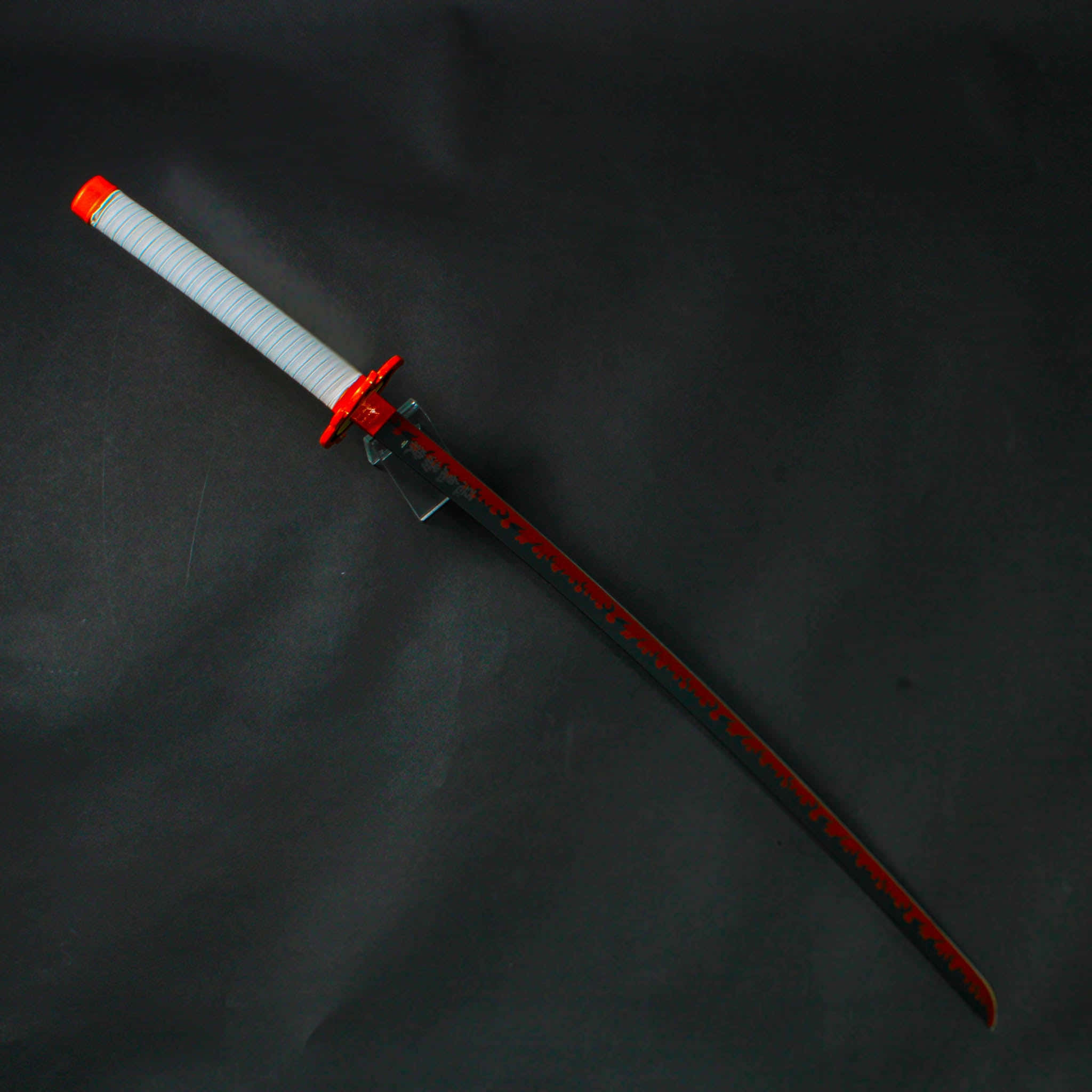 Nichirin Blades 桌布 壁紙 — 一把帶有紅色點綴和白色纏柄的武士刀，斜放在深色紋理表面上。