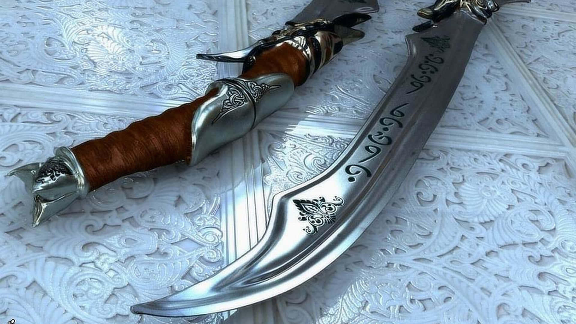 Ancient Weapons 桌布 壁紙 — 一把彎曲華麗的銀劍，帶有棕色皮革握把，放置在白色雕刻裝飾表面上。