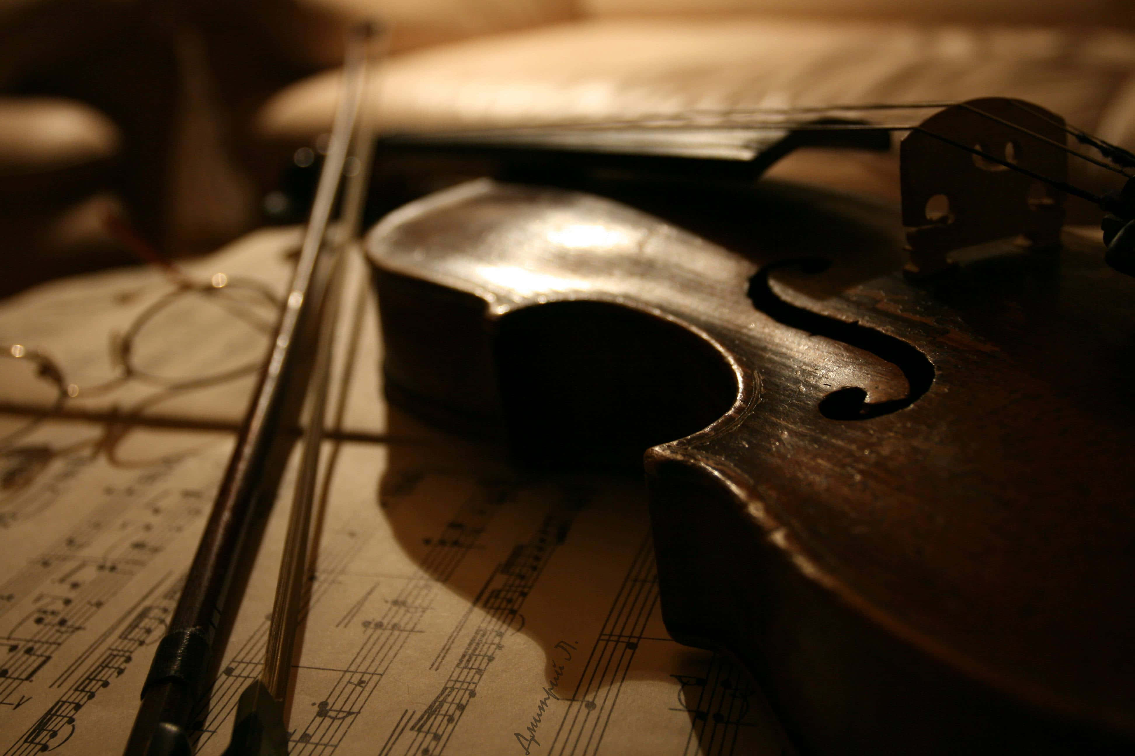 Classical Music 桌布 壁紙 — 一把復古小提琴和琴弓在泛黃的樂譜上溫暖地照亮，營造出舒適親密的氛圍。