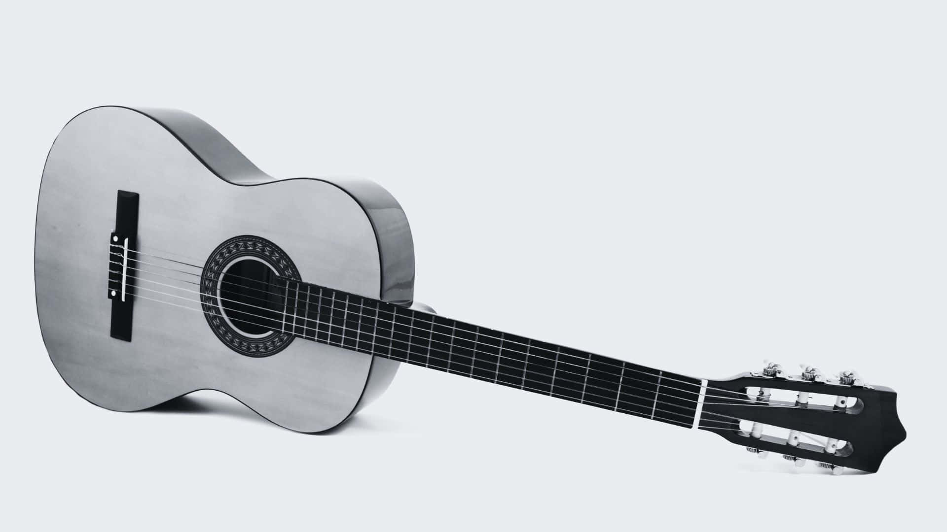 Black And White Guitar 桌布 壁紙 — 一把時尚的銀色古典結他斜靠在柔和的灰色背景上，展現其優雅的曲線和深色指板。