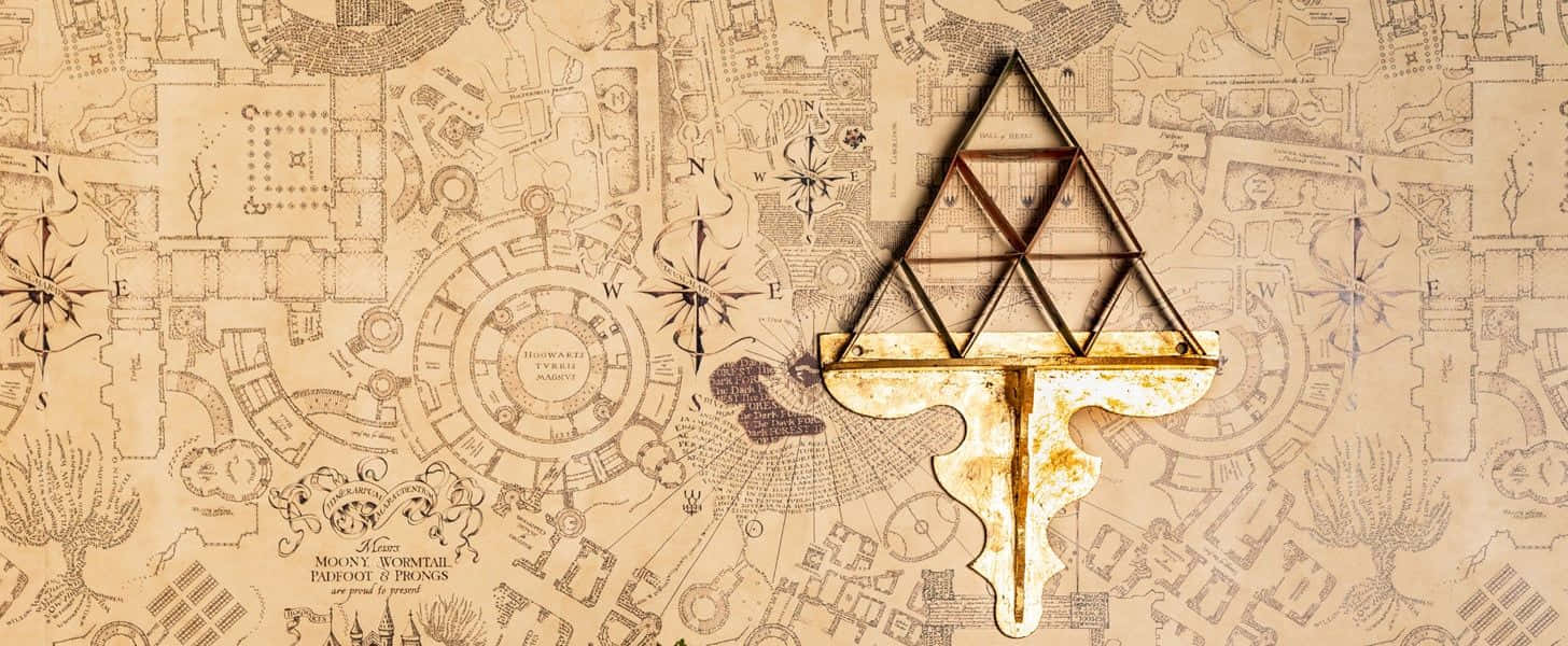 The Marauder's Map 桌布 壁紙 — 一把生鏽的三角形鑰匙放在一幅帶有指南針和詳細建築的霍格華茲古老羊皮紙地圖上。