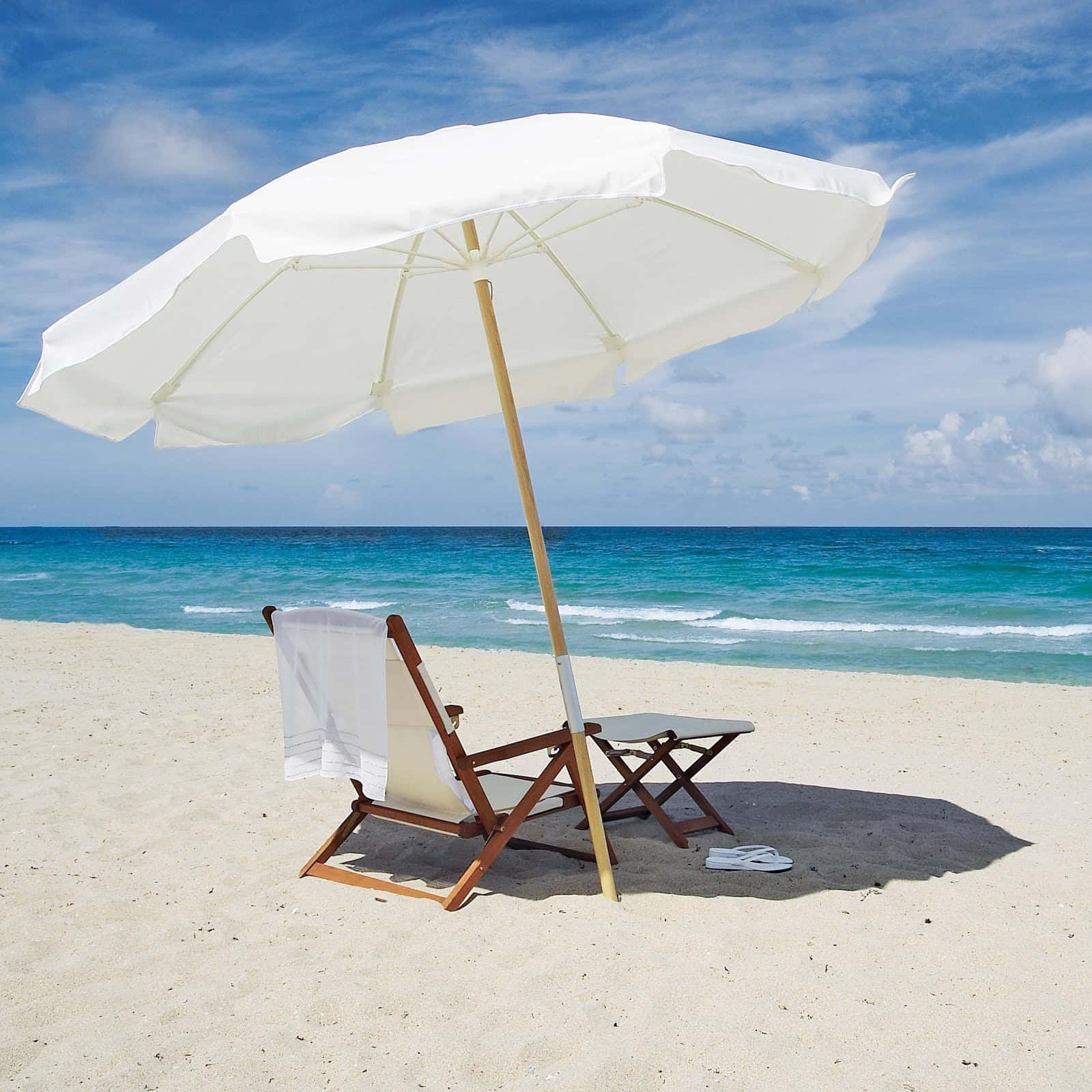 Beach Umbrella 桌布 壁紙 — 一把白色沙灘傘為一張木製躺椅和小桌子在陽光明媚的沙灘上遮蔭，背景是碧綠的海浪。