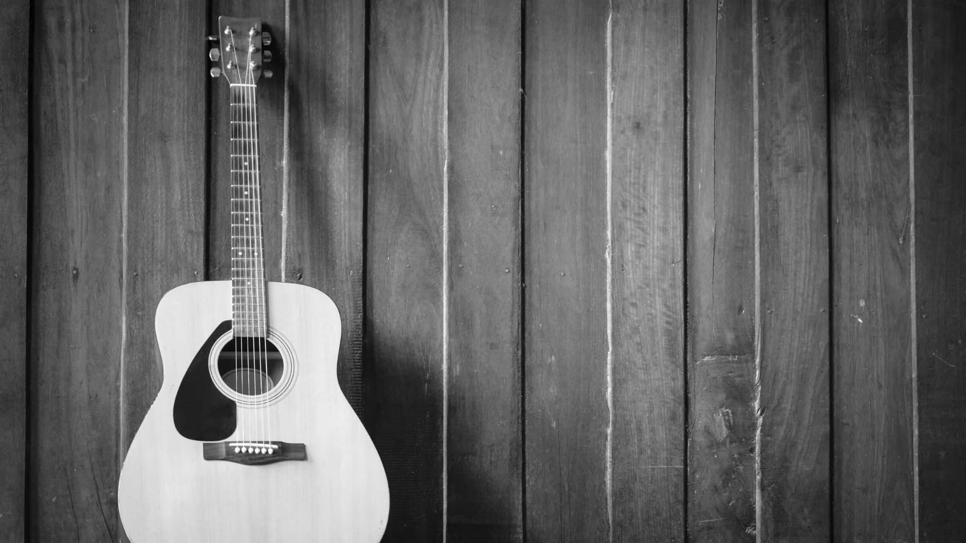 Black And White Guitar 桌布 壁紙 — 一把經典木結他掛在風化的木牆上，以黑白呈現，喚起質樸的音樂懷舊感。