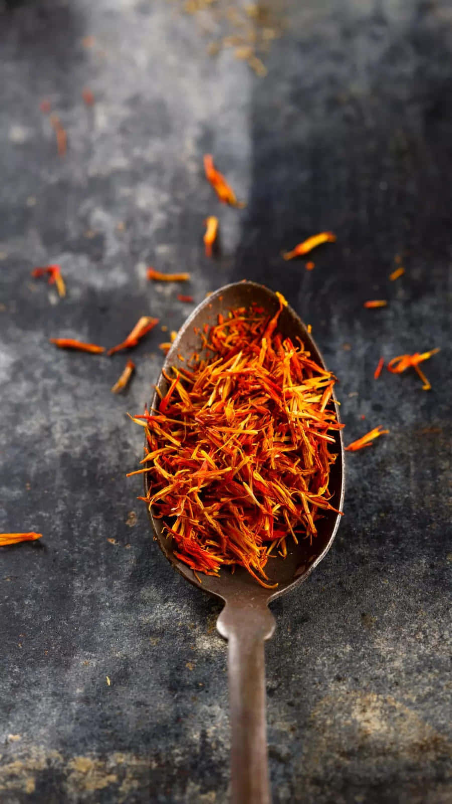 Saffron 桌布 壁紙 — 一把質樸的湯匙盛滿鮮豔的橙色番紅花絲，放在深色紋理表面上，周圍散落著絲線。