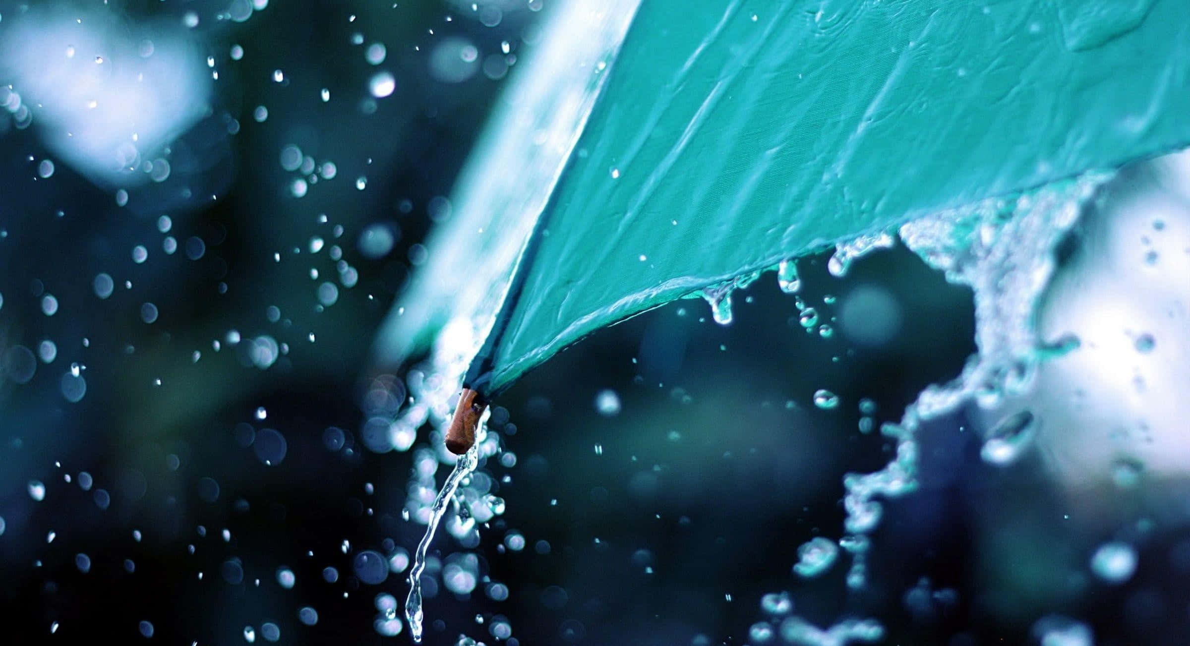 Rainy 桌布 壁紙 — 一把青綠色雨傘在模糊的黑暗背景和散景燈光中滴下水珠。