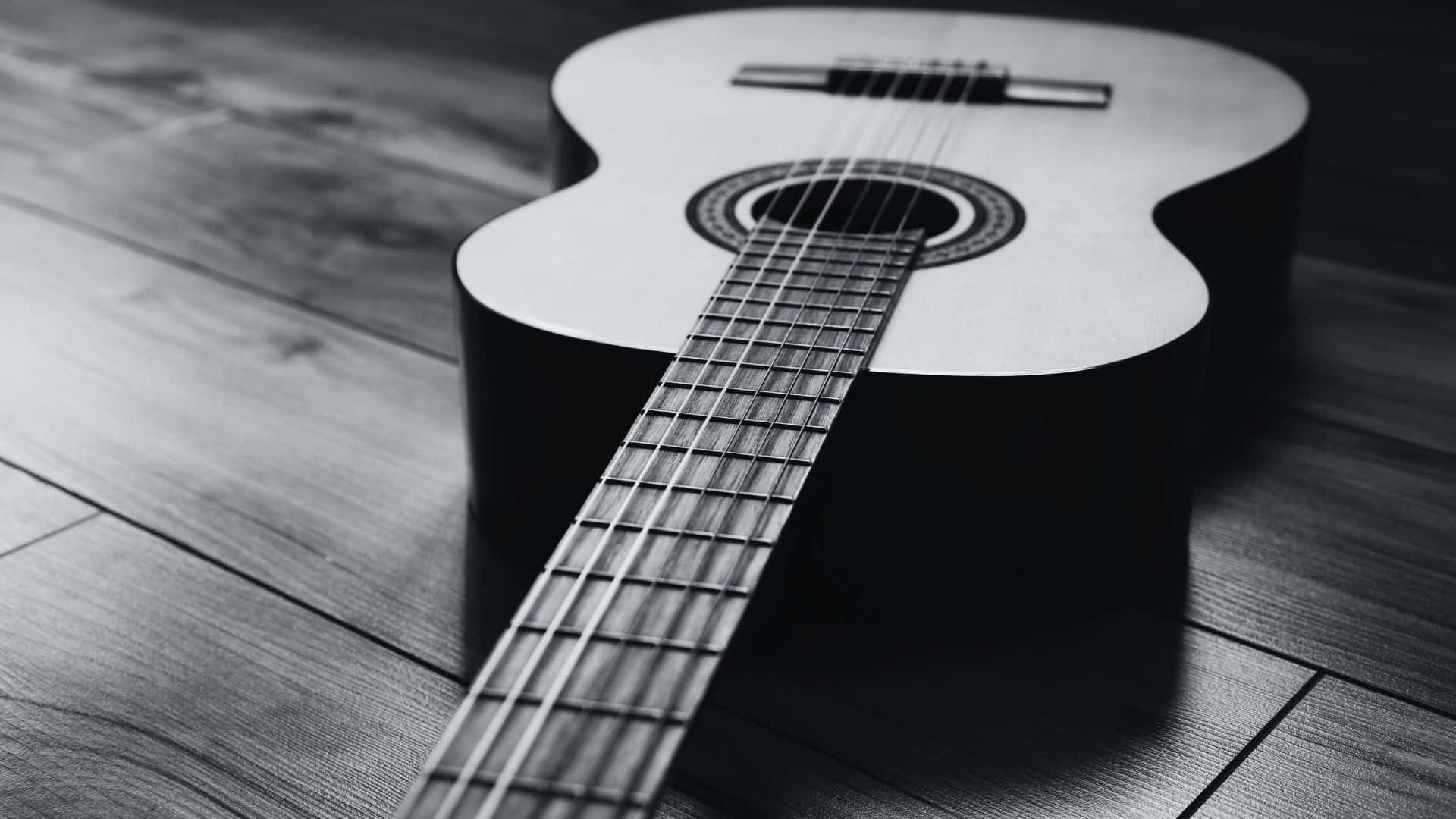 Black And White Guitar 桌布 壁紙 — 一把黑白原聲結他斜放在木地板上，帶有戲劇性的陰影。