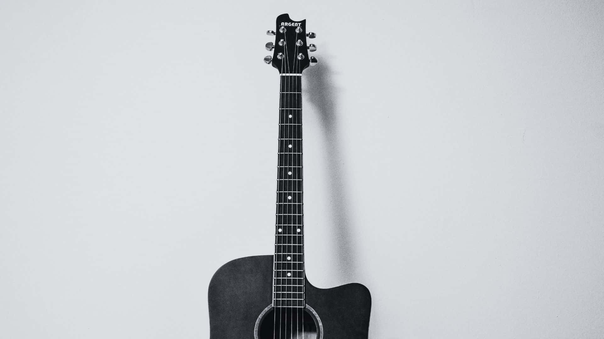 Black And White Guitar 桌布 壁紙 — 一把黑色木結他垂直掛在純淺灰色牆上，投下柔和陰影。