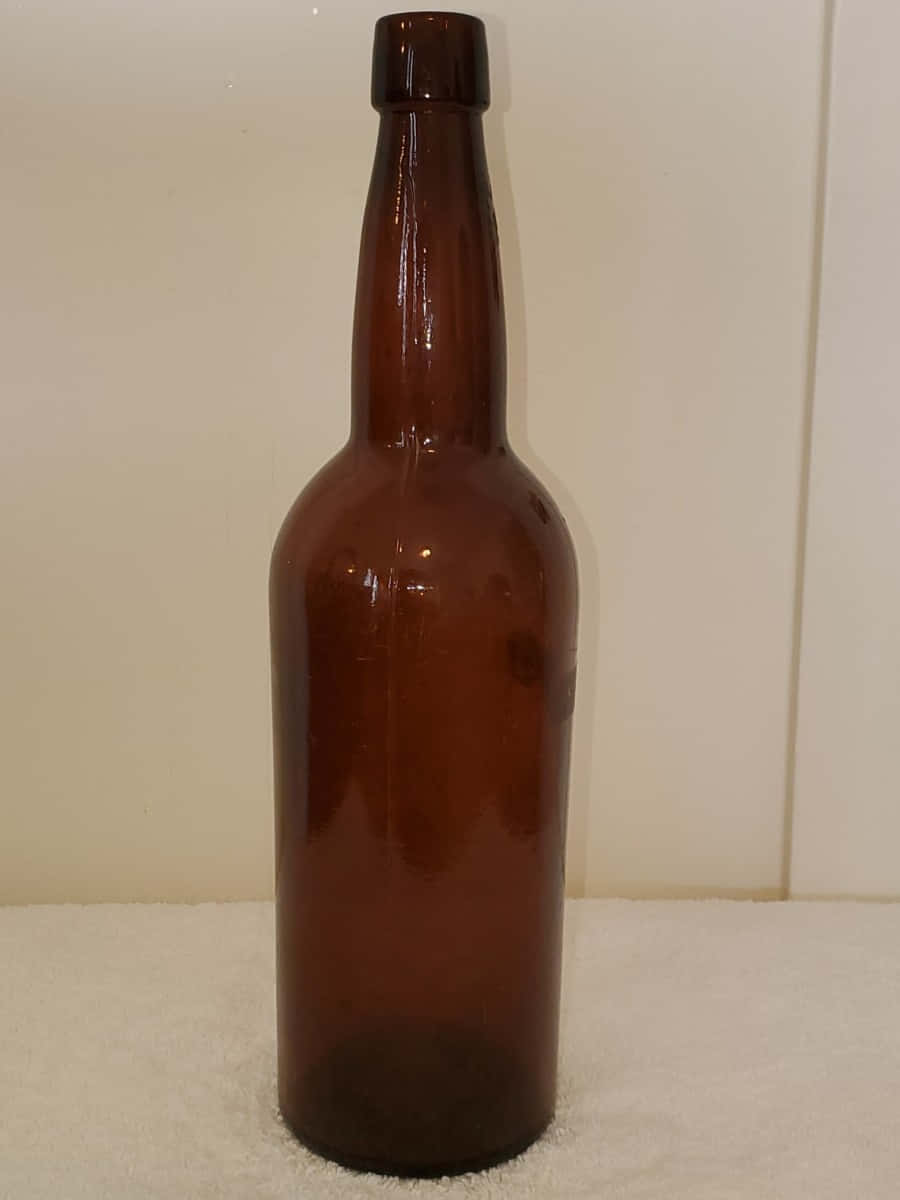 一排古董葡萄酒瓶 壁紙 — 一個高身琥珀色玻璃瓶，長頸，直立於白色紋理表面上，背景為素色牆壁。