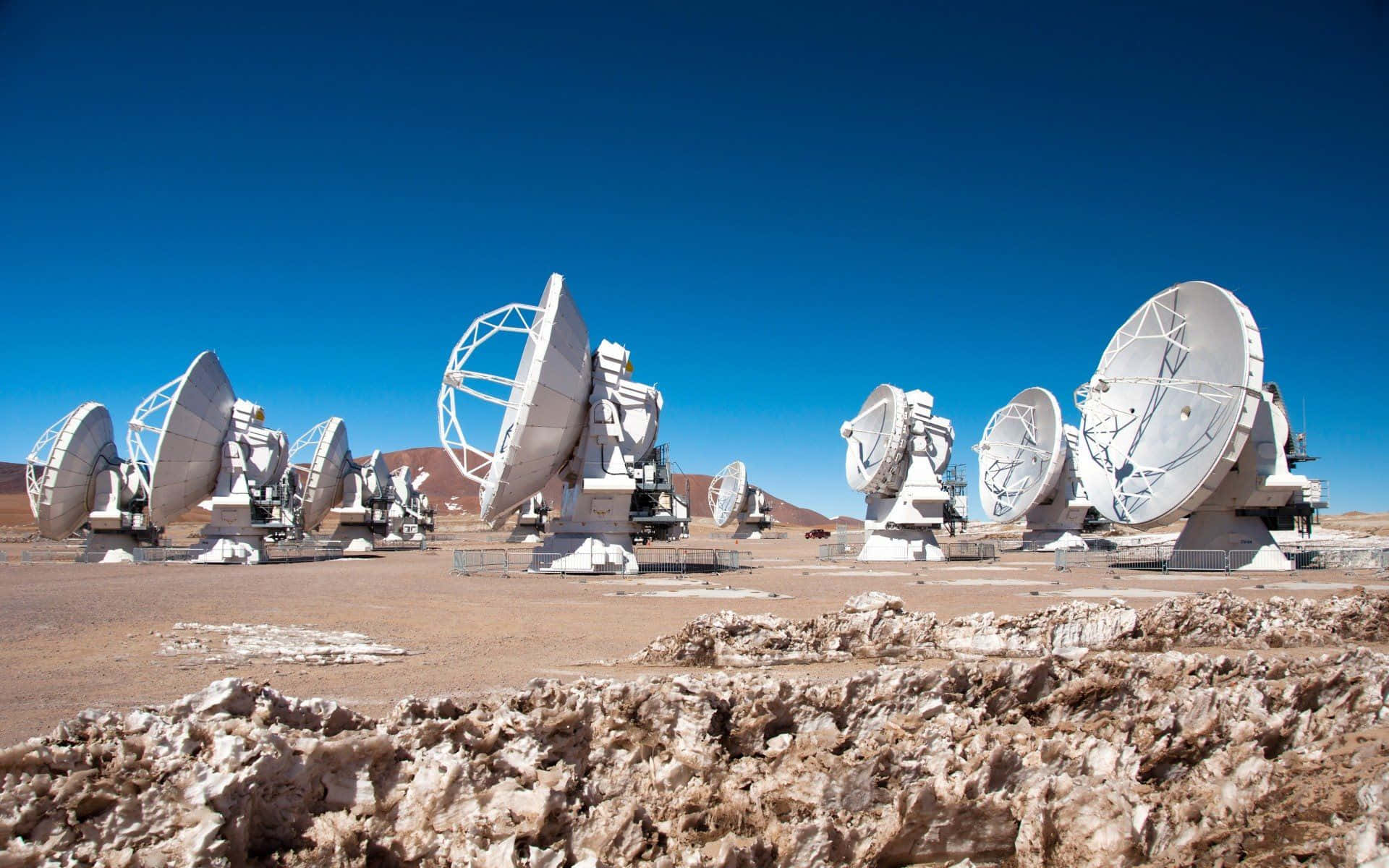 Radio Telescope 桌布 壁紙 — 一排大型白色無線電望遠鏡矗立在晴朗藍天下嘅貧瘠沙漠中。