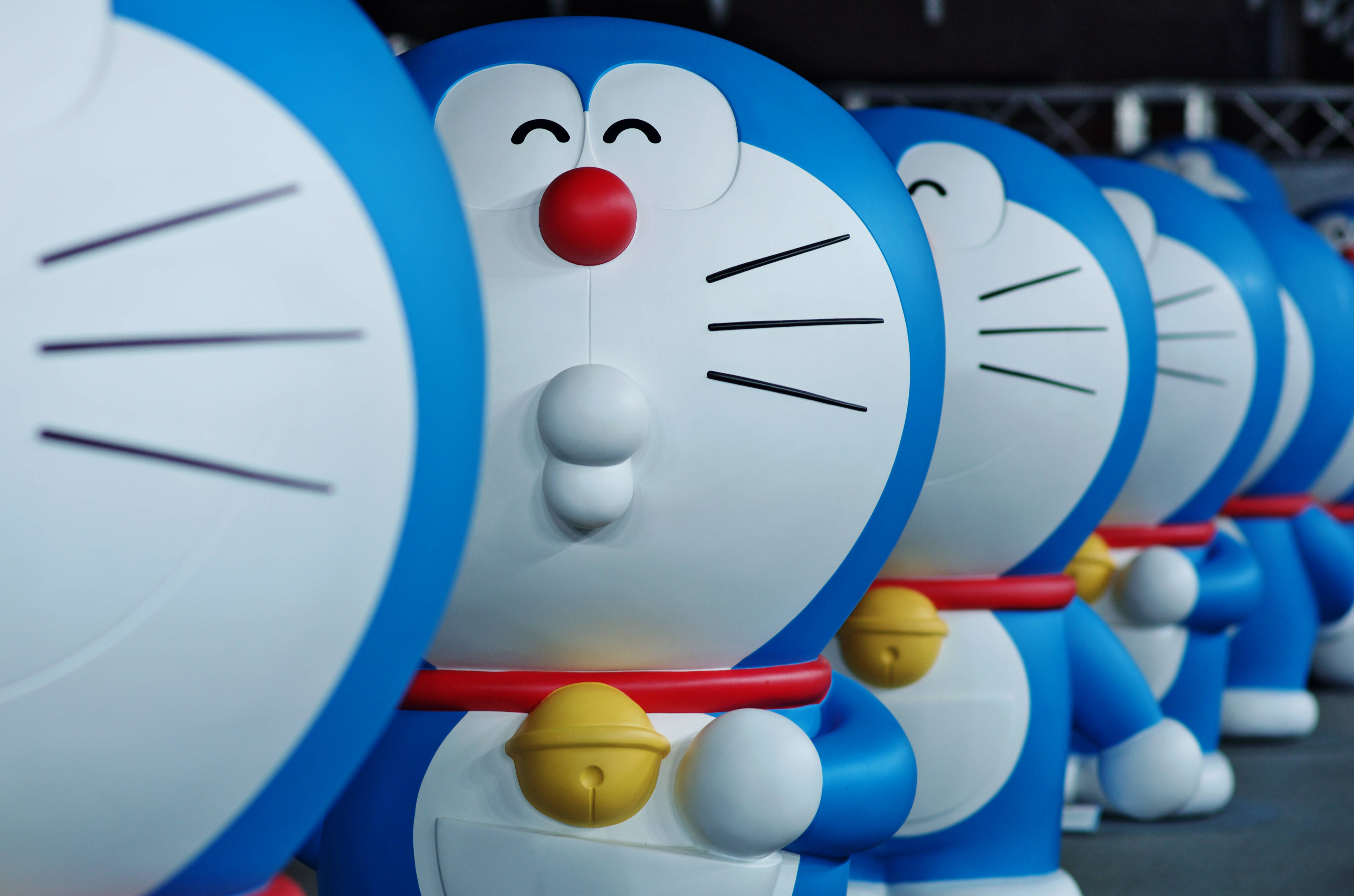 Doraemon 桌布 壁紙 — 一排大型藍白色多啦A夢雕像，紅色鼻子和黃色鈴鐺，處於淺景深中。