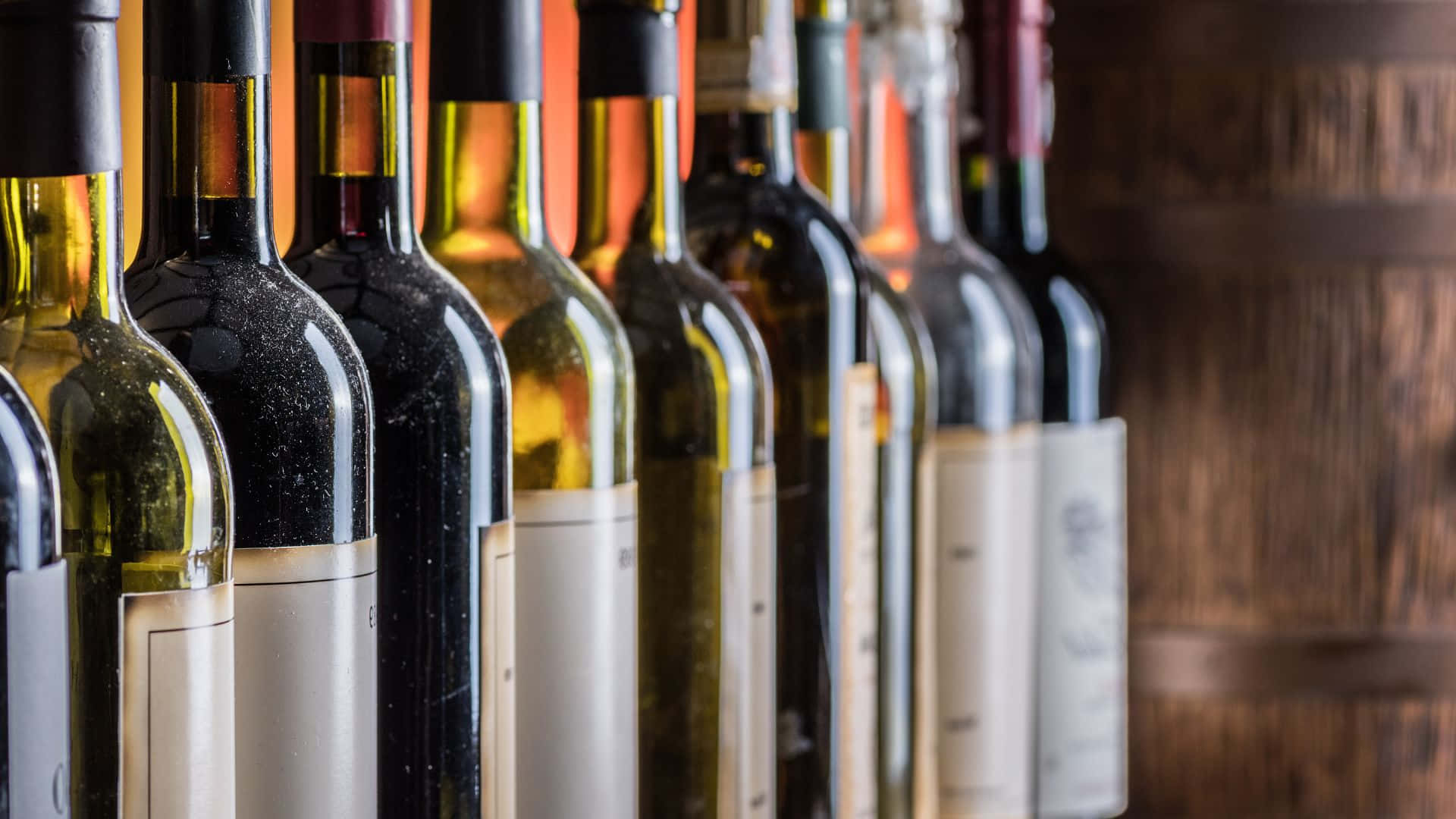 1920 X 1080 桌布 壁紙 — 一排帶有不同標籤和顏色的酒瓶，在溫暖的環境光線下站在木桶前。