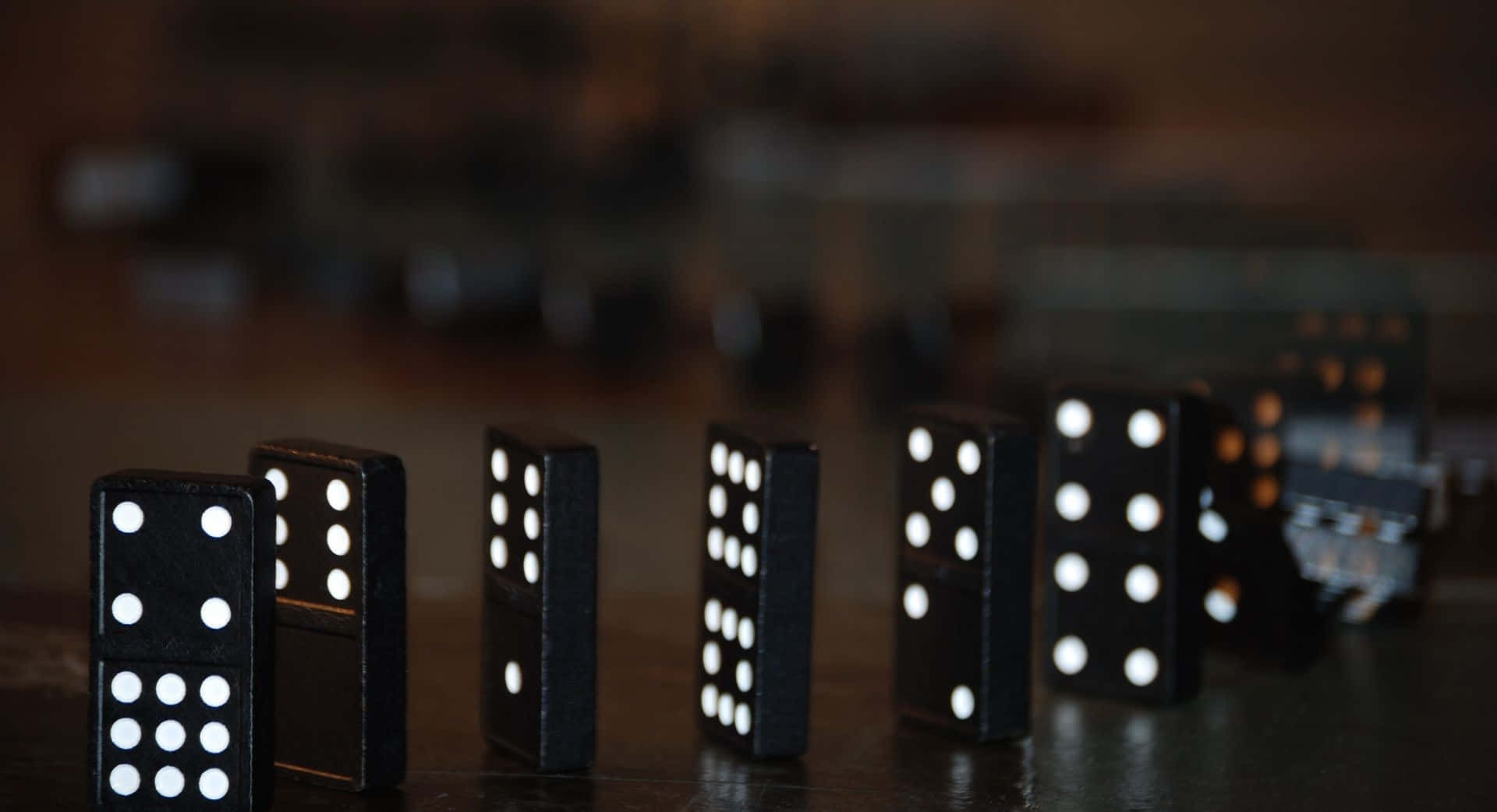 Domino 桌布 壁紙 — 一排帶有白色圓點的黑色多米諾骨牌直立於深色木質表面上，景深較淺。