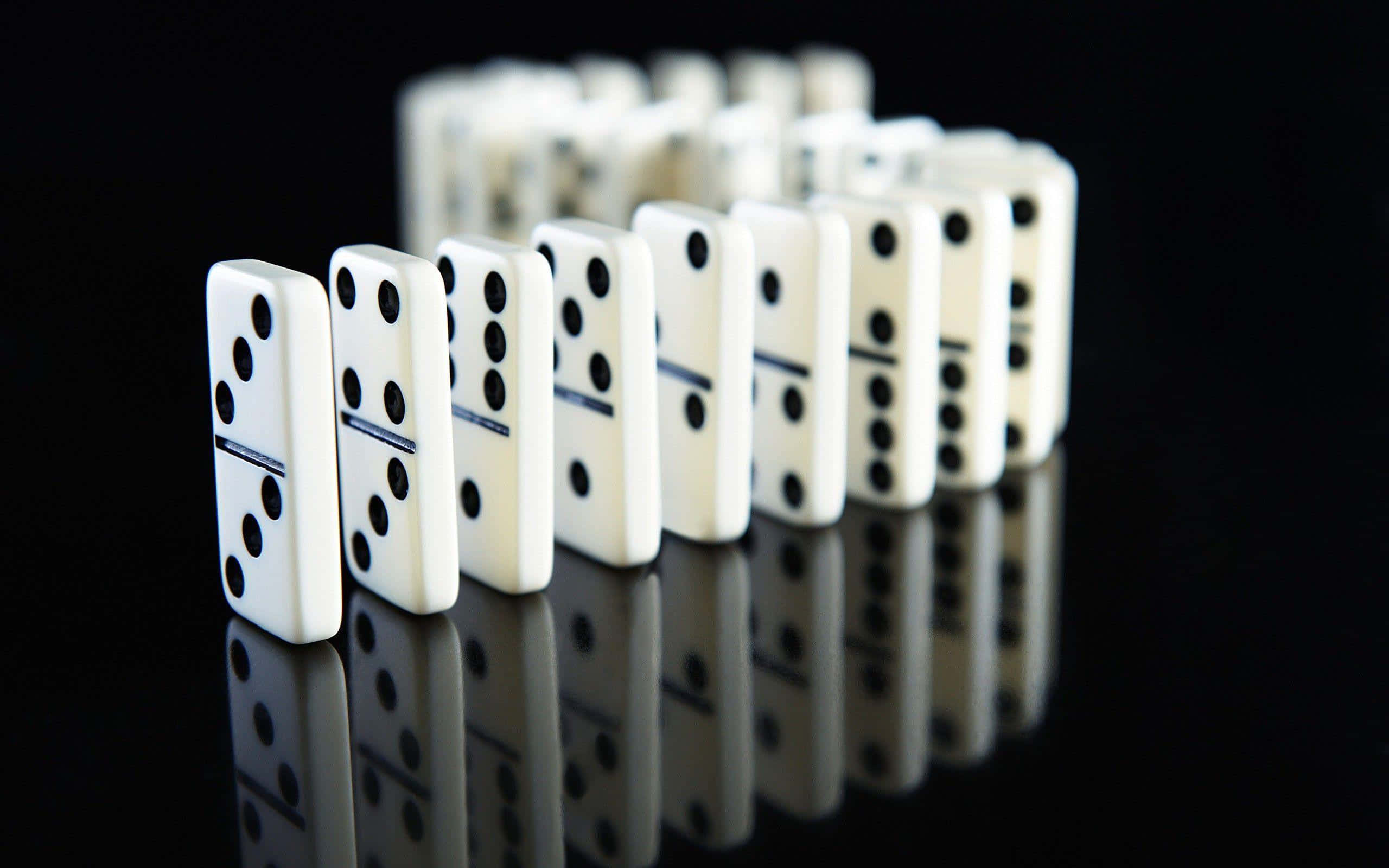 Domino 桌布 壁紙 — 一排帶有黑色點的白色的多米諾骨牌豎立在反光的黑色表面上，營造出鏡面效果。