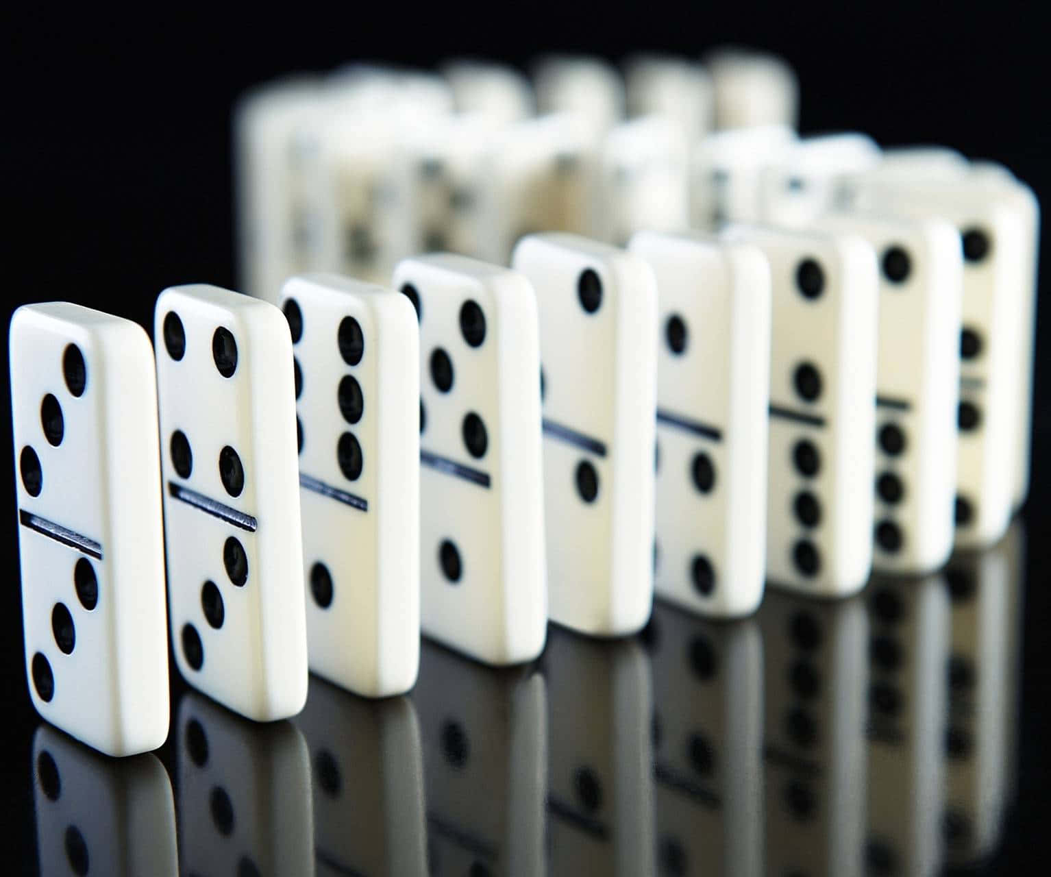 Domino 桌布 壁紙 — 一排帶有黑點的白色的多米諾骨牌豎立在反光的黑色表面上，形成鮮明對比和淺景深。