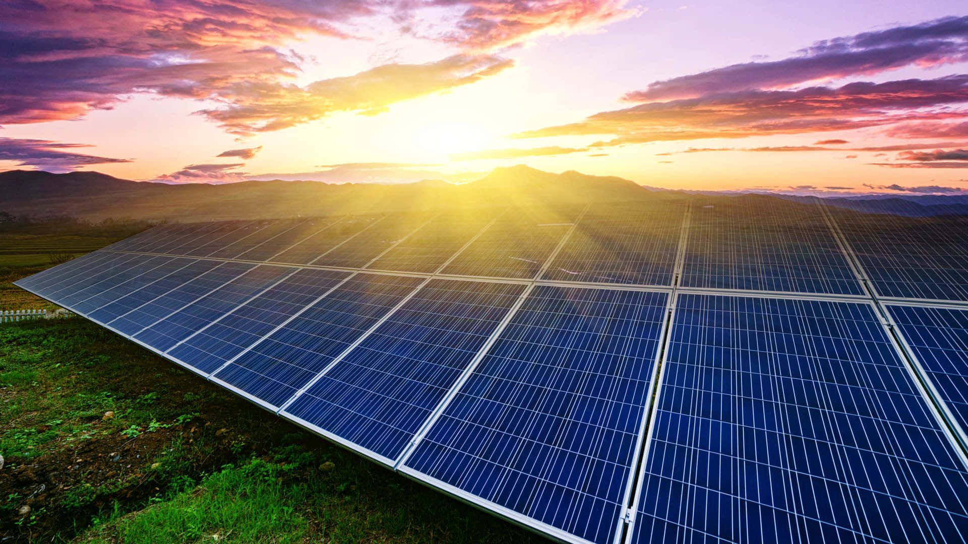 Energy 桌布 壁紙 — 一排排太陽能板在充滿活力的日落天空下閃耀，天空有紫橙色雲彩和遠山。