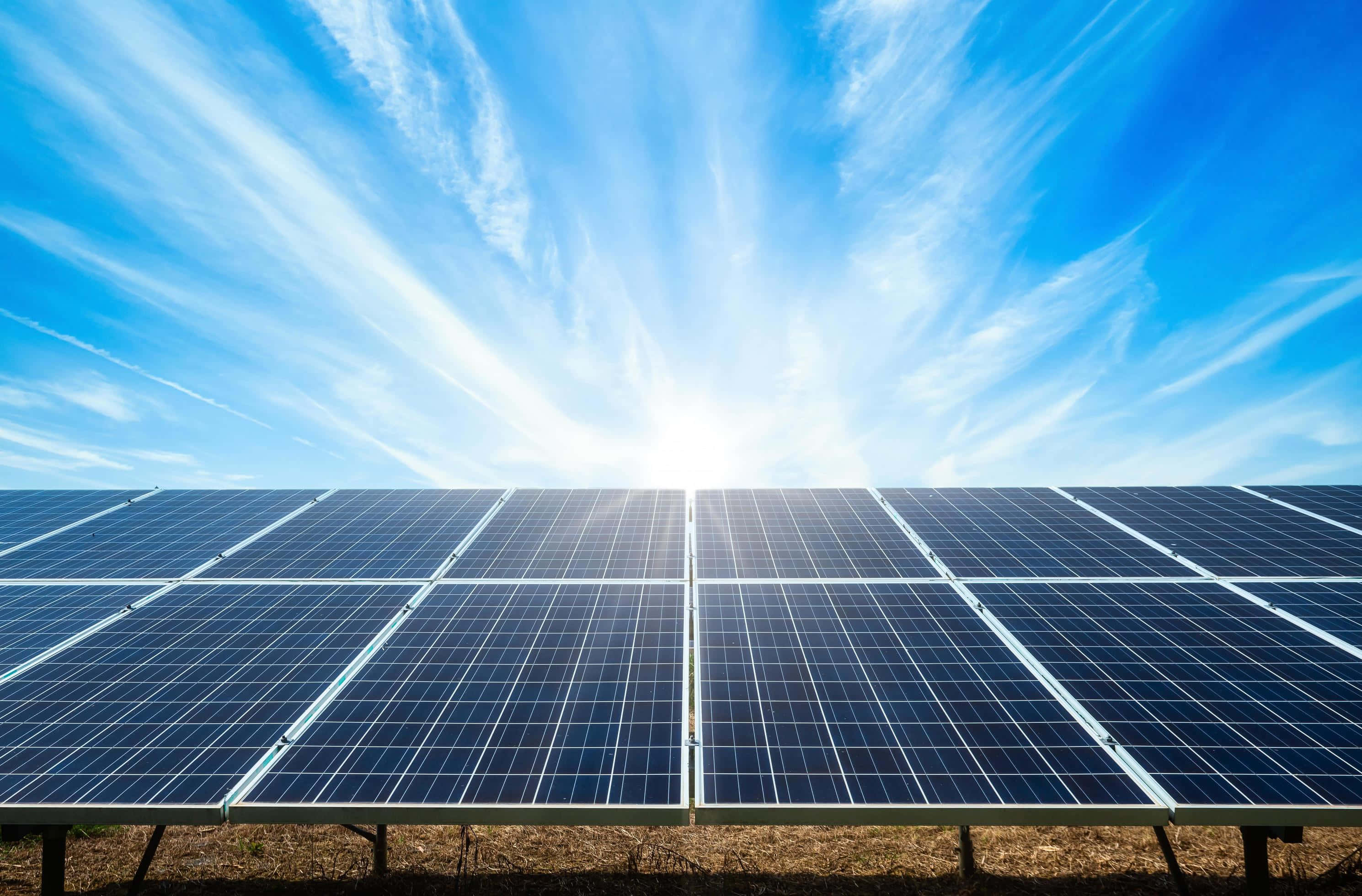 Solar Panel 桌布 壁紙 — 一排排太陽能板在明亮的藍天下延伸，伴隨著縷縷白雲和燦爛的陽光。